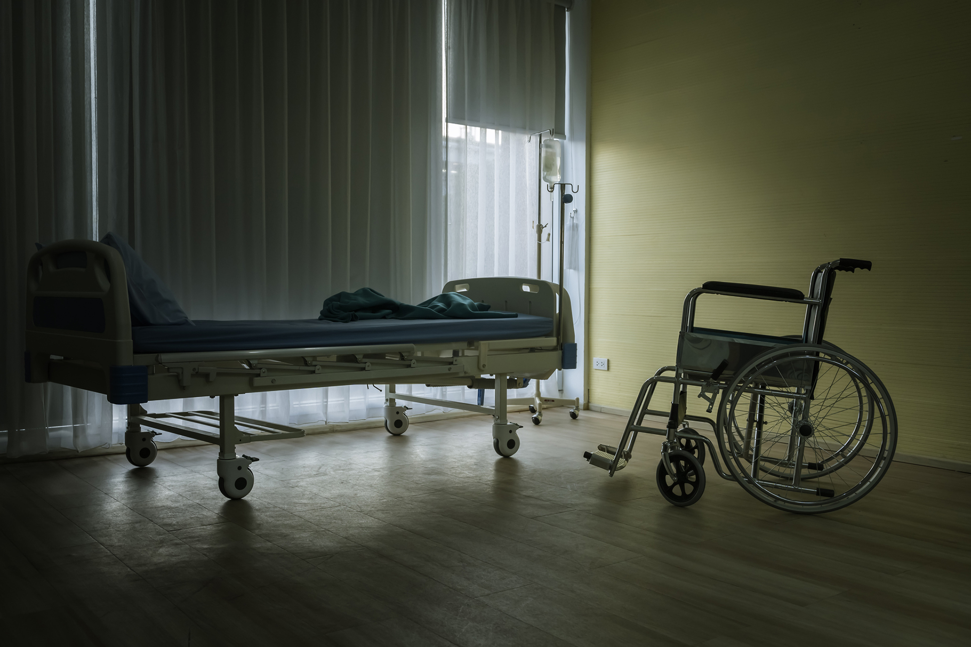 Empty hospital bed and wheelchair in a health care facility with curtains drawn.