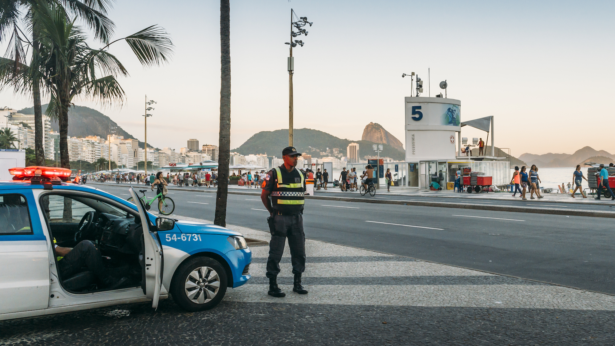Police officer stands in front of his car on a street near the ocean boardwalk in Rio de Janeiro, Brazil
