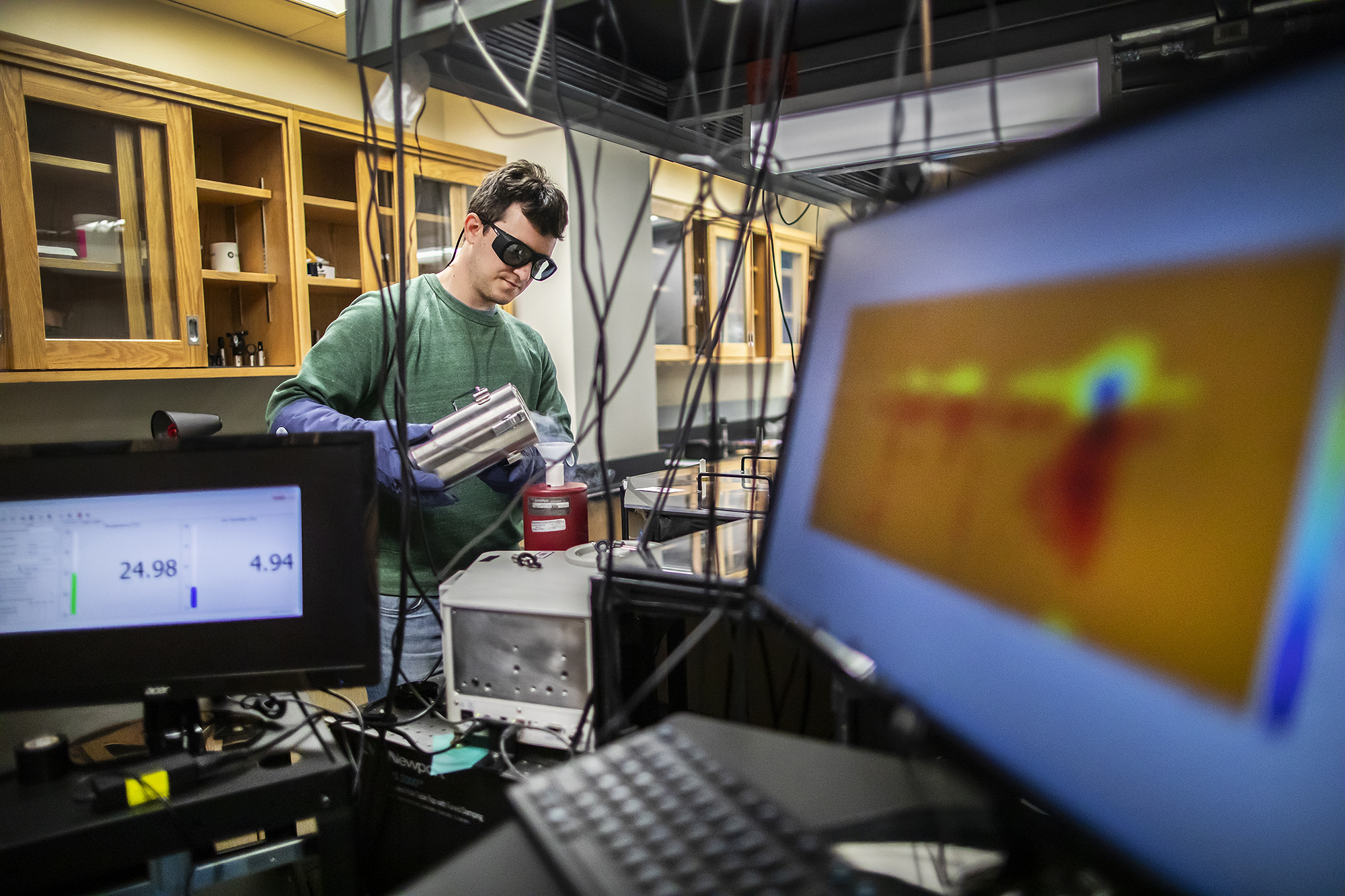 Student führt chemische Forschung im Labor durch, eingerahmt von Computerbildschirmen und anderen Geräten.