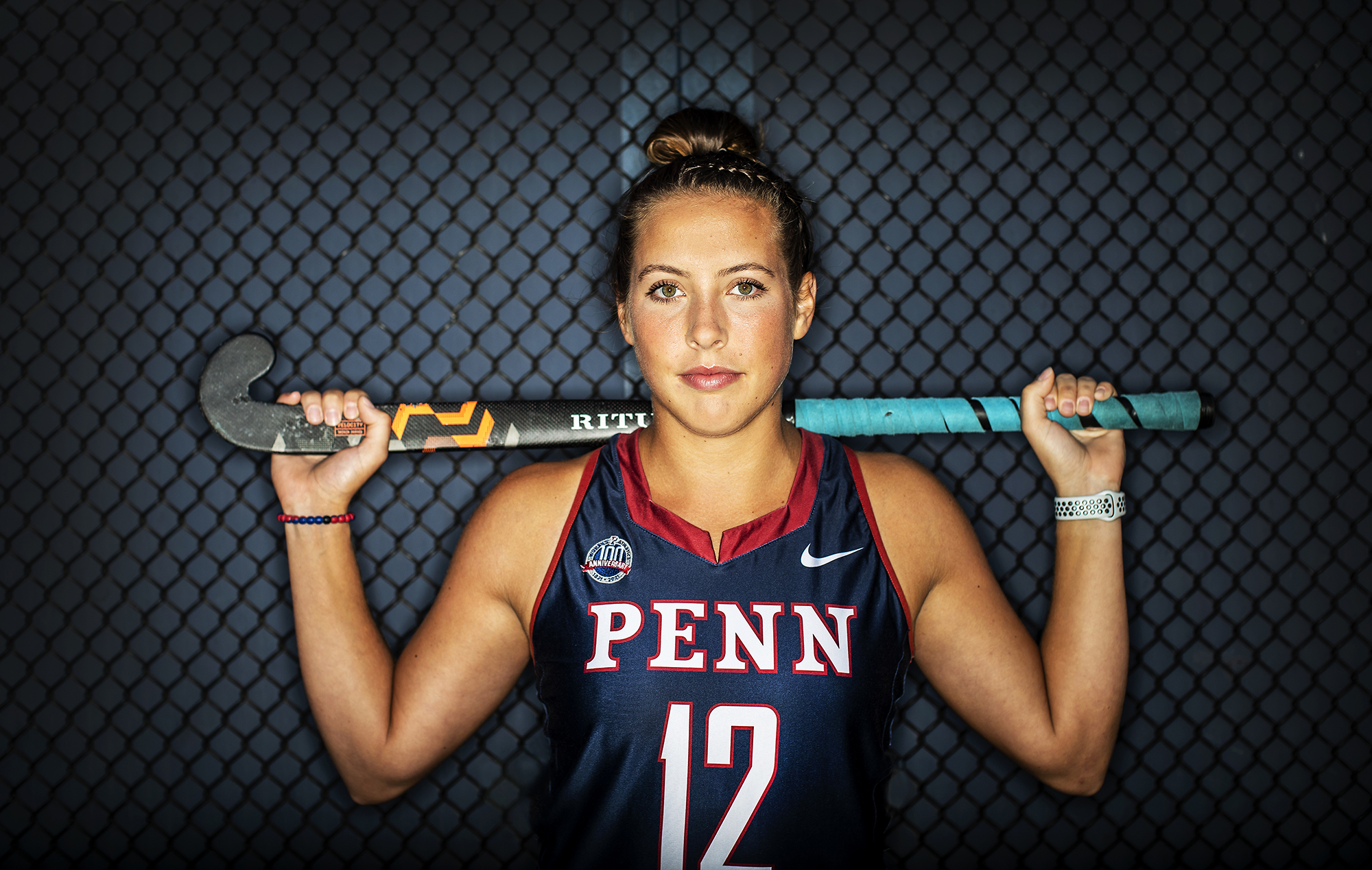 Banks holds her field hockey stick along her shoulders behind her neck.