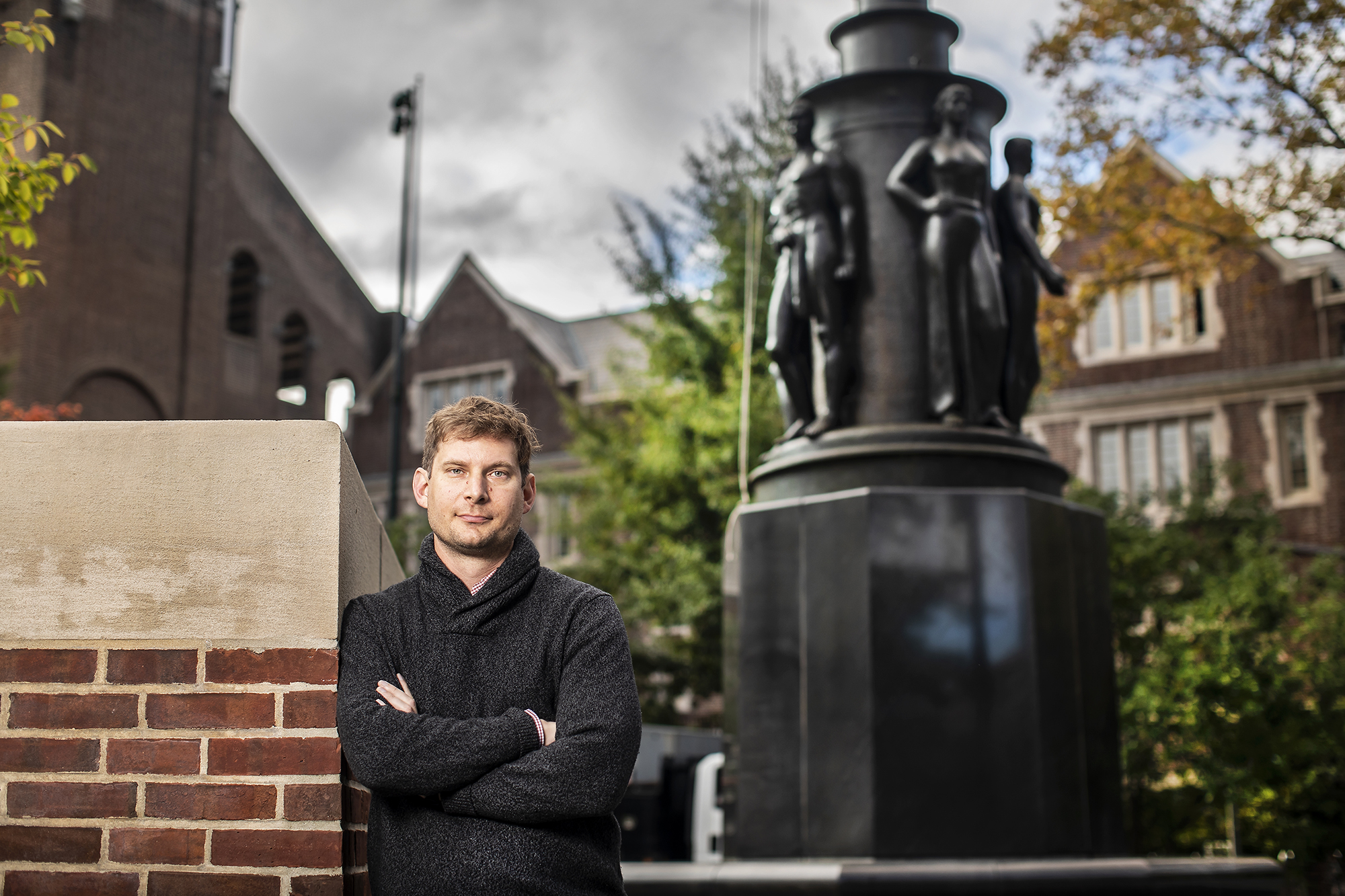 Jason Hartwig stands with arms crossed in front of a statue on Penn’s campus.