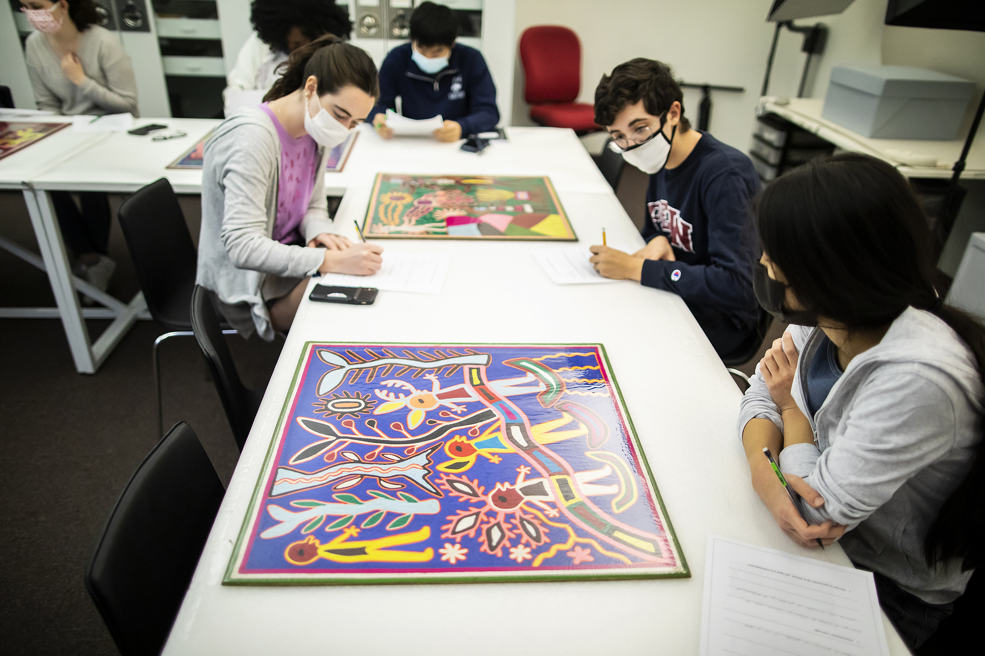 four students at a long table looking at colorful artworks 