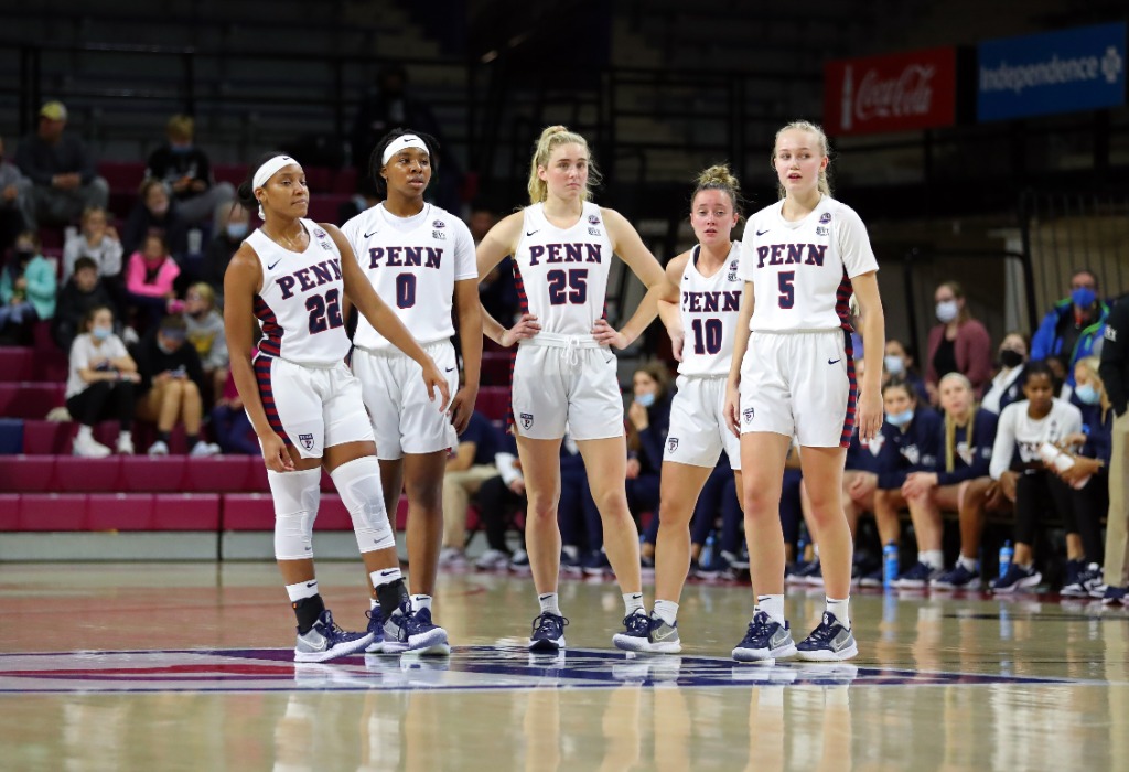 Five members of the women's basketball team stand together at center court at the Palestra.