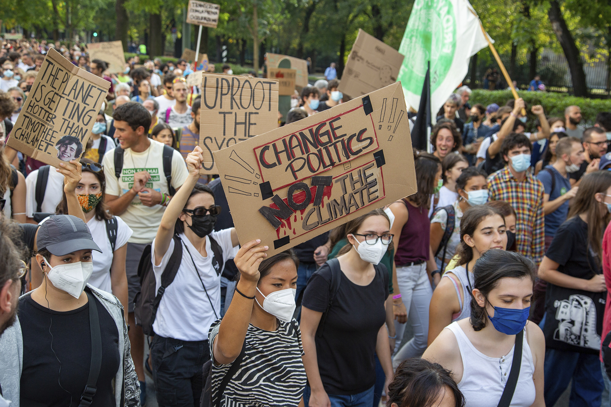 A masked crowd of protesters marching holding cardboard signs, one reads CHANGE POLITICS NOT THE CLIMATE.