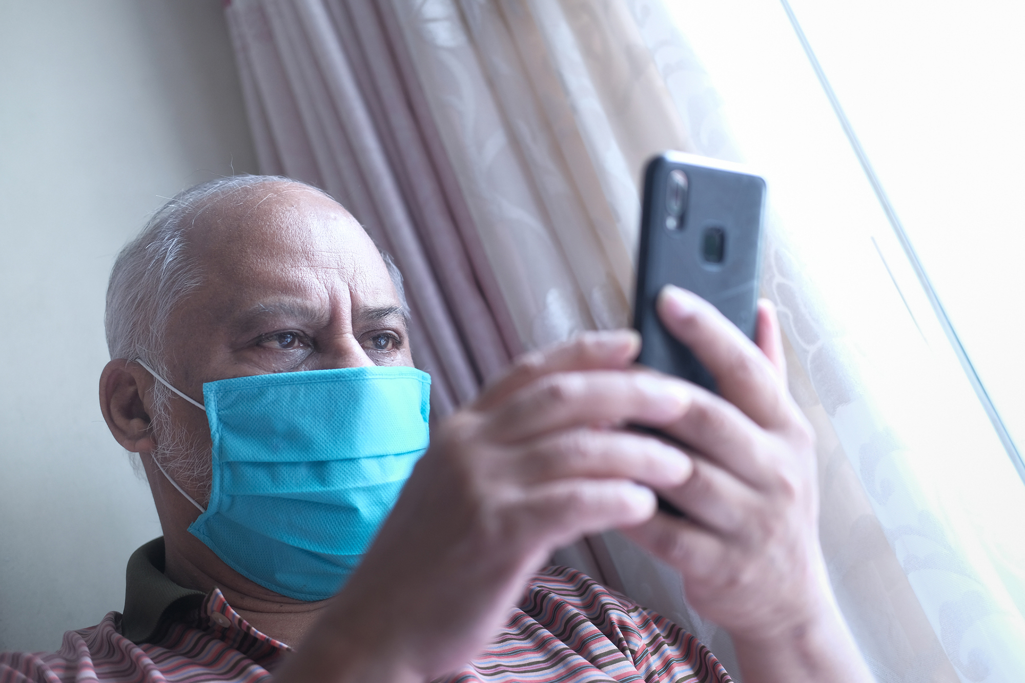 Person wearing a face mask holds up a smartphone, reading a text message.