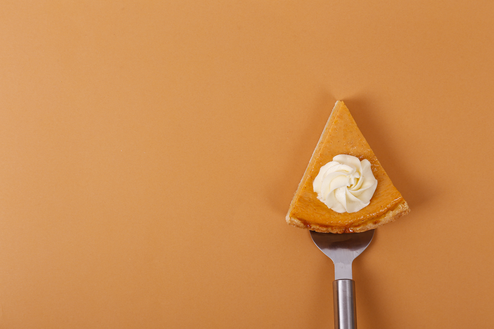 A piece of pumpkin pie on a serving spatula, a dollop of whipped cream on top. 