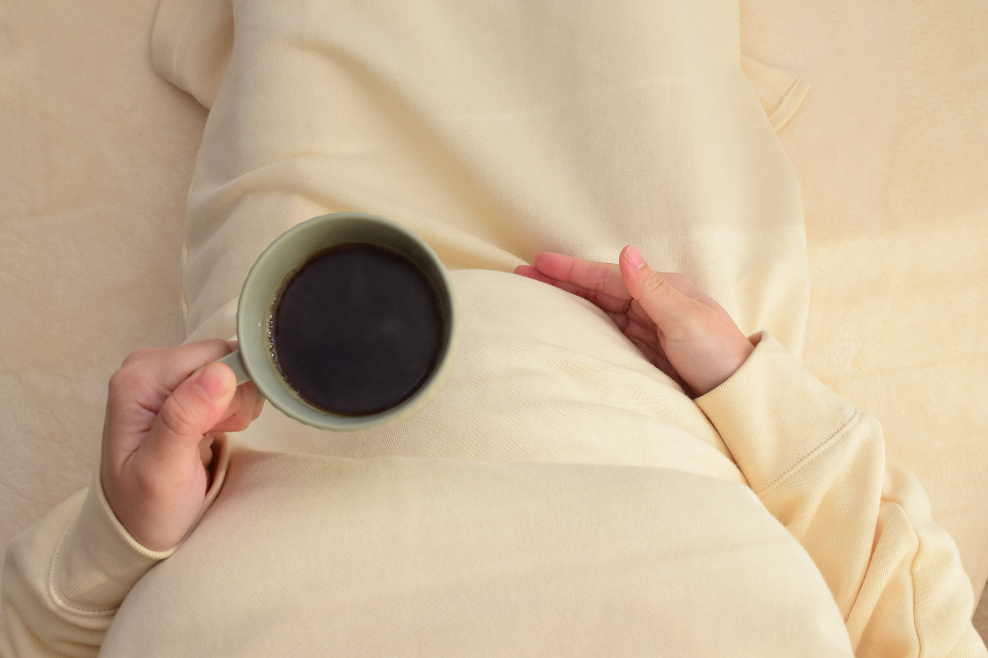 Mug of coffee resting on a third-trimester pregnant belly.