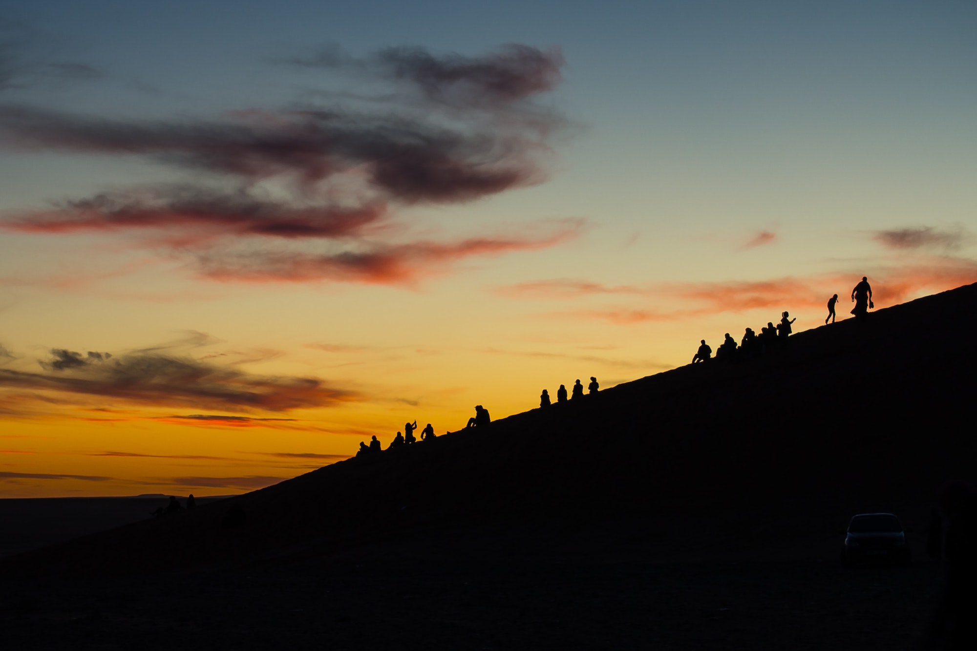 People silohetted against a hill at sunset