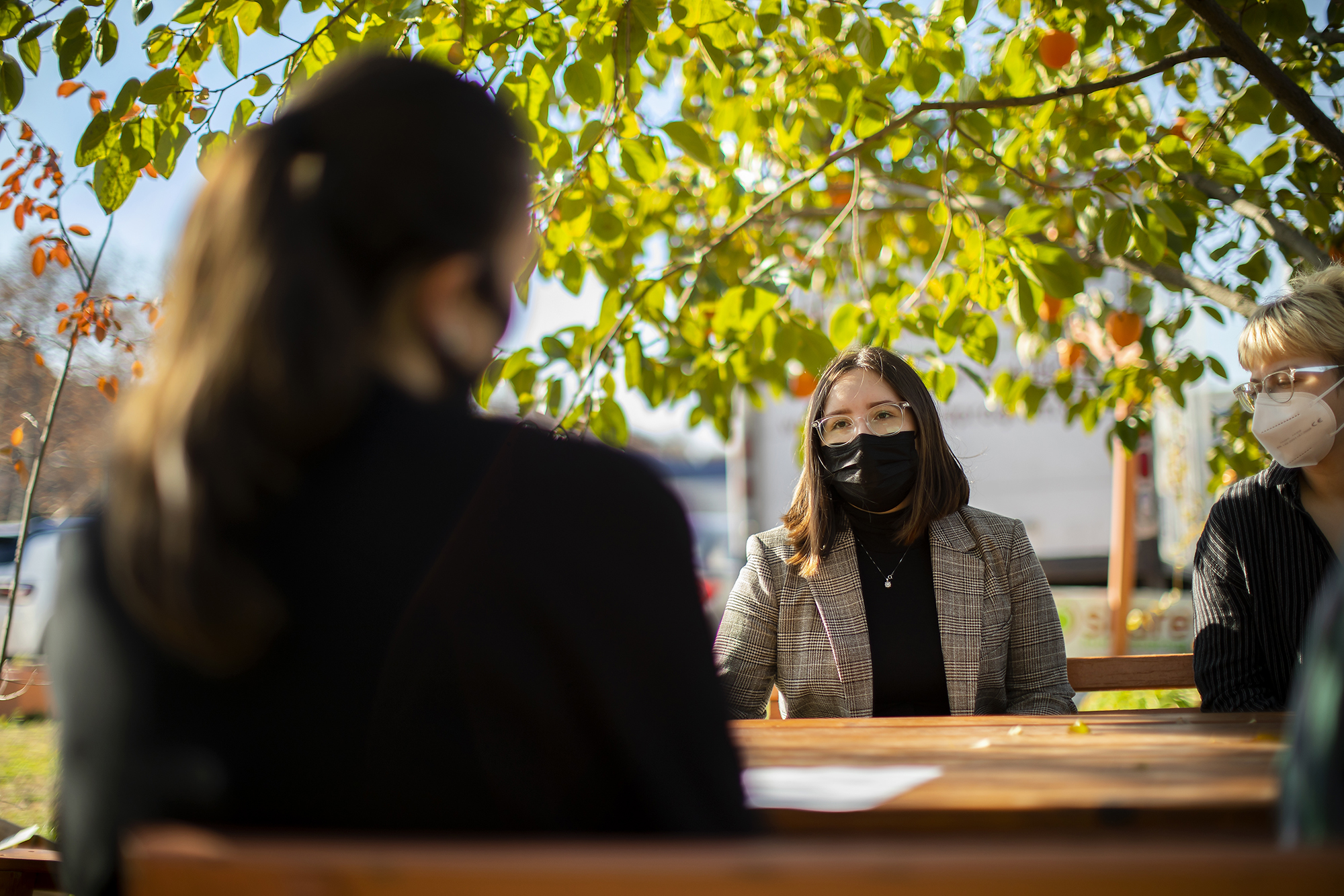 People sit at picnic table in face masks on a fall day