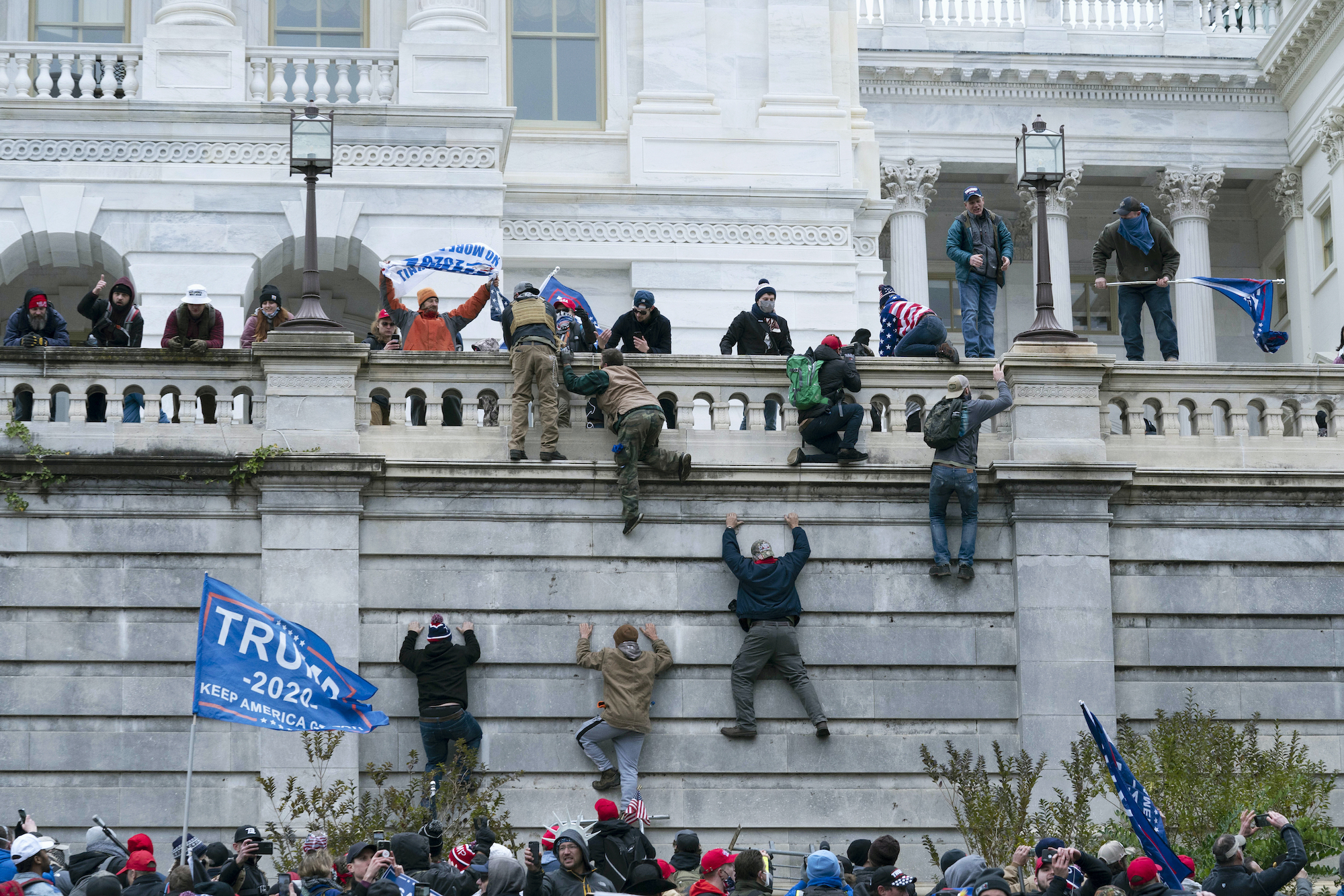 Supporters of Donald Trump scale a wall at the U.S. Capitol as Trump flags wave