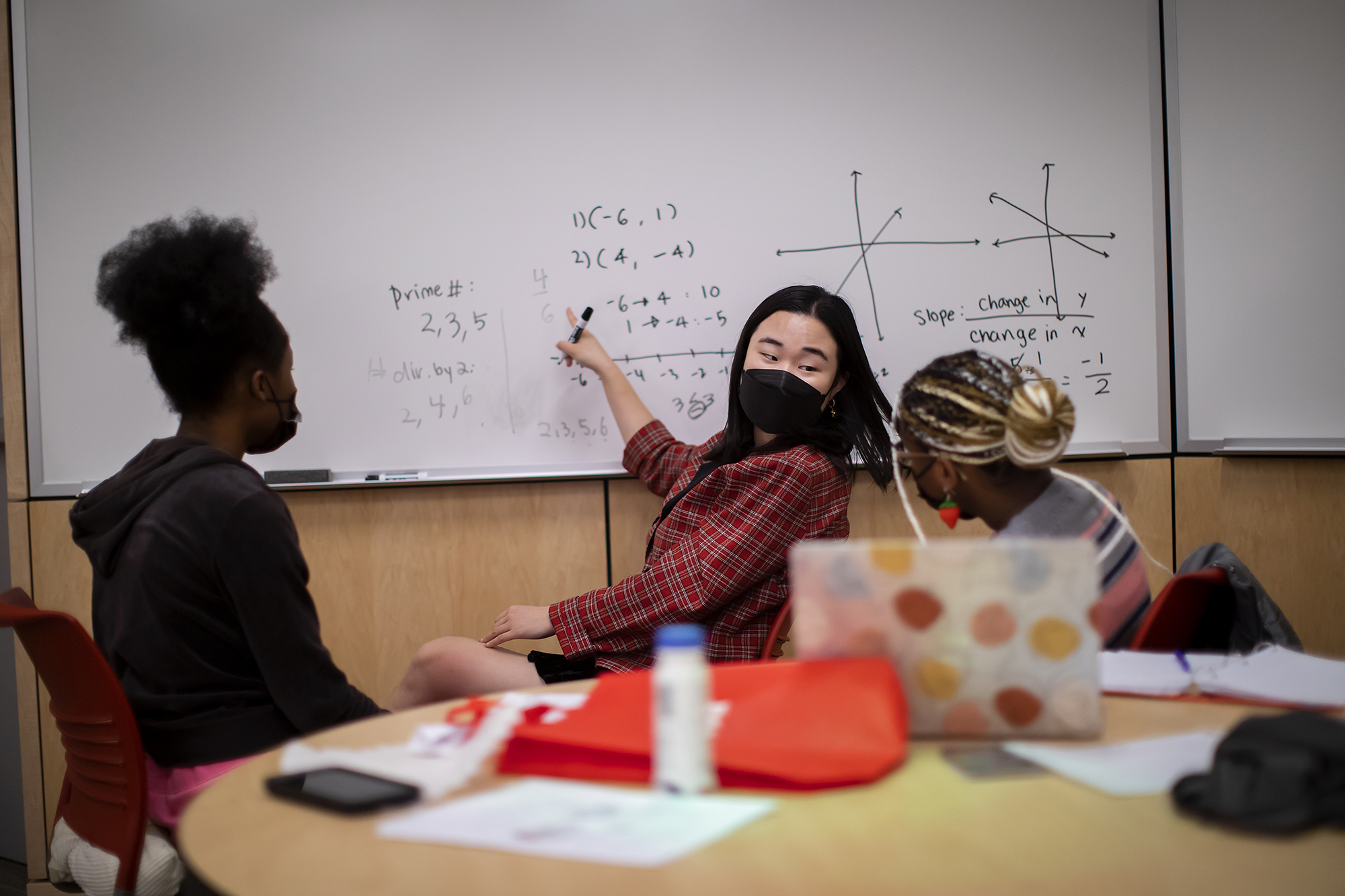 two people looking at a student who is pointing at a math equation on a white board