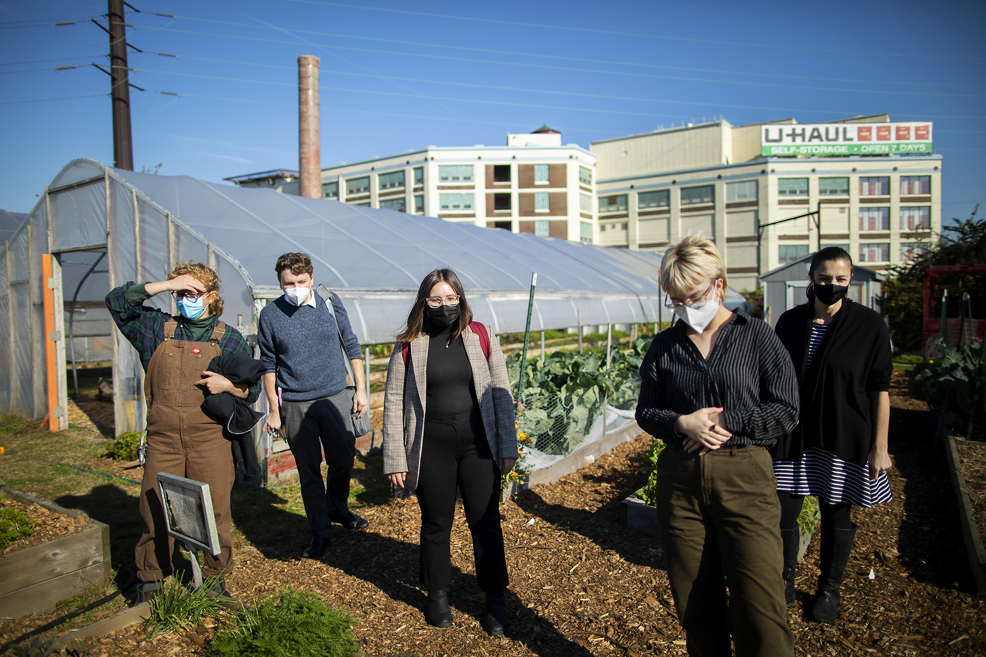 Five people stand in an urban garden with storage facilities in the background