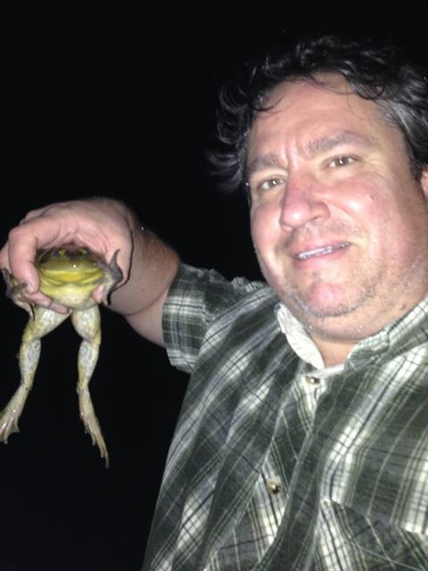A person holding a bullfrog, whose legs are dangling. 