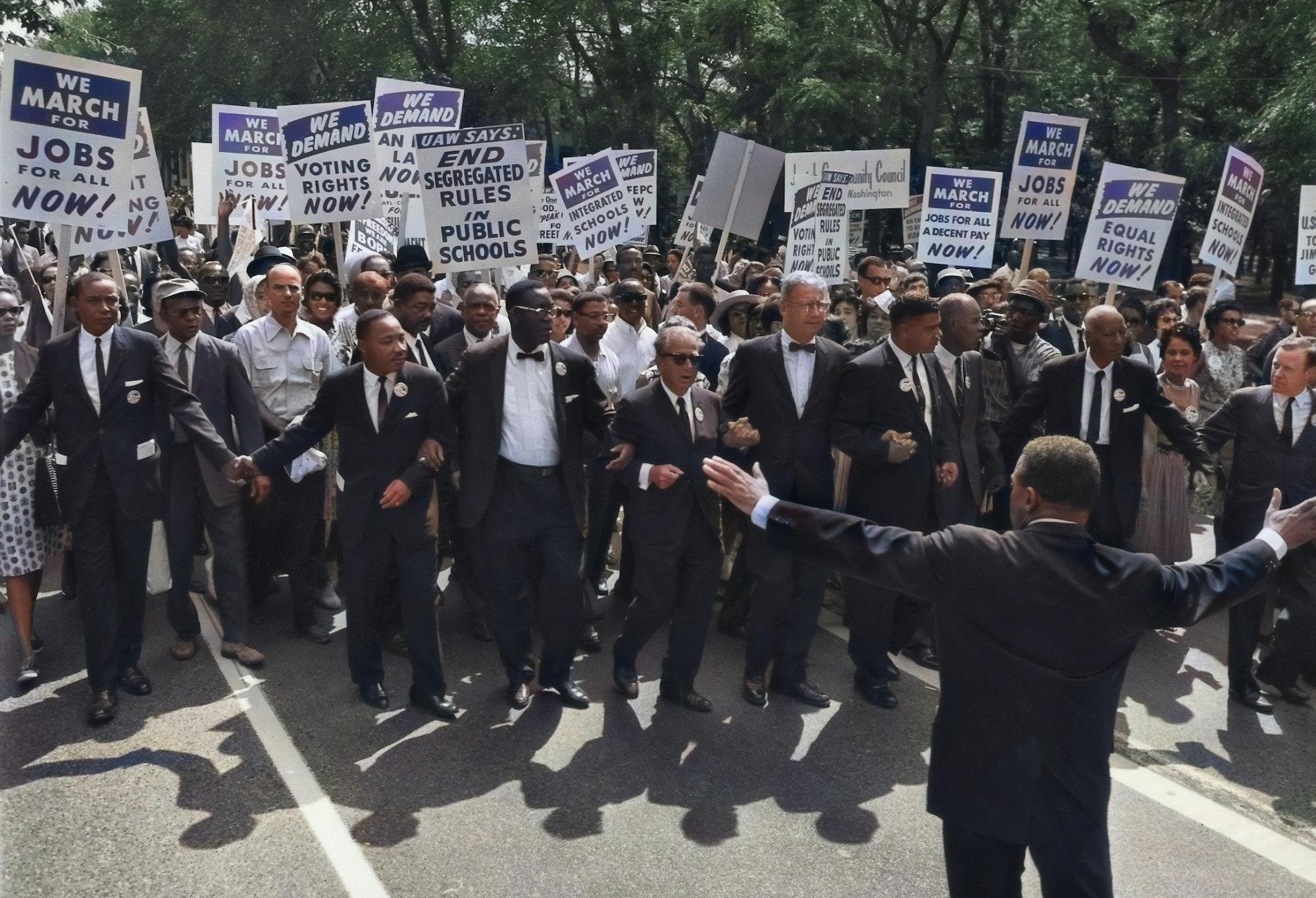 People march waving signs that say "end segregated rules in public schools" and "we demand voting rights now"