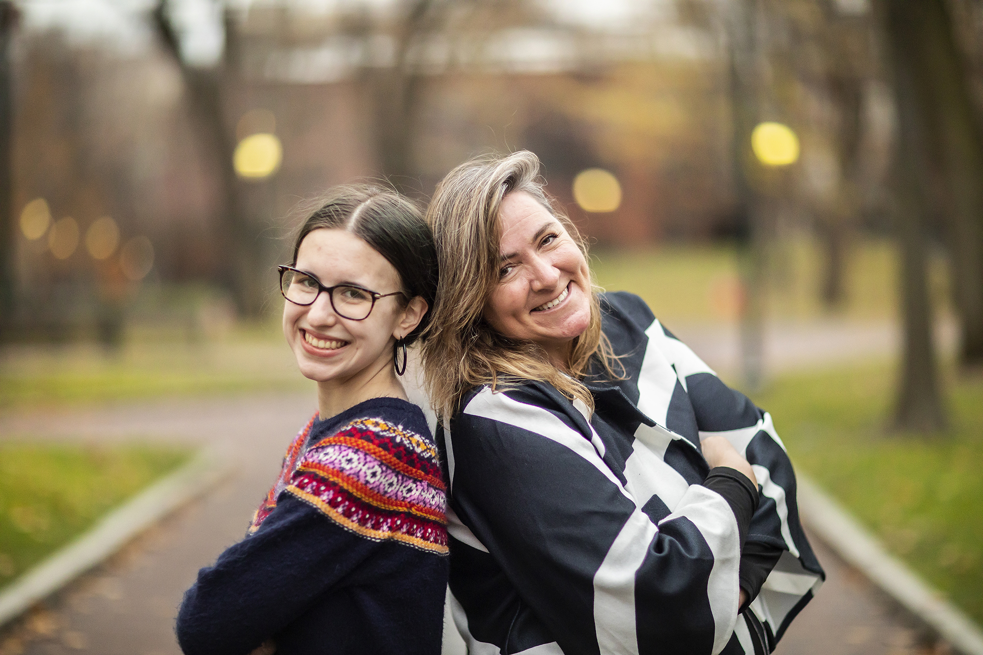 two people standing outside back to back smiling at camera