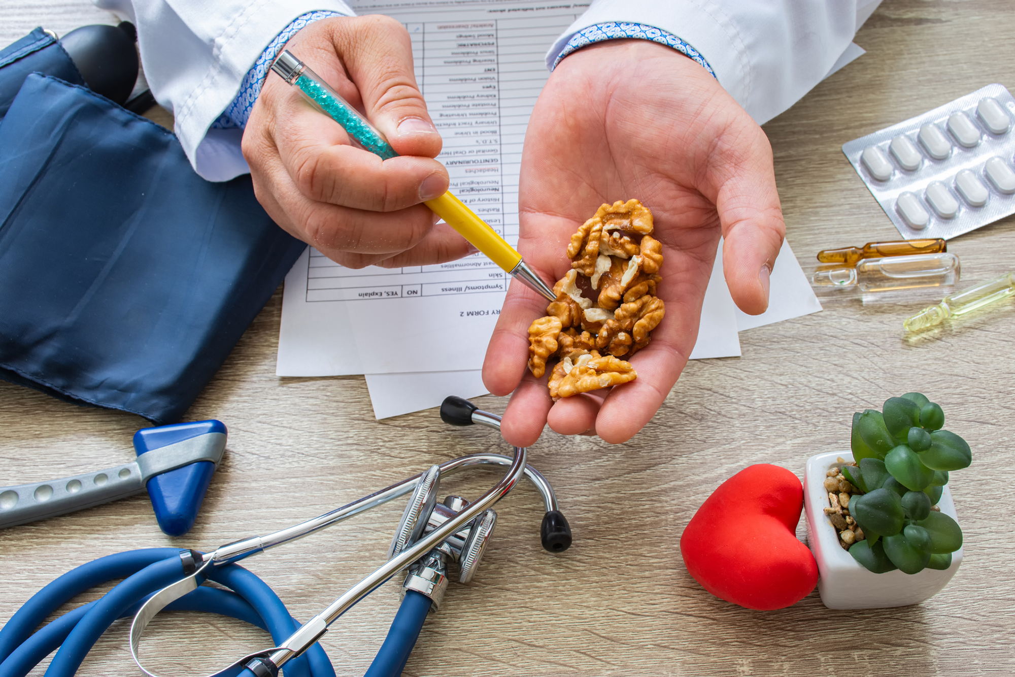 Dietician pointing to a handful of walnuts with a blood pressure cuff, paperwork, and a stethoscope on the table.