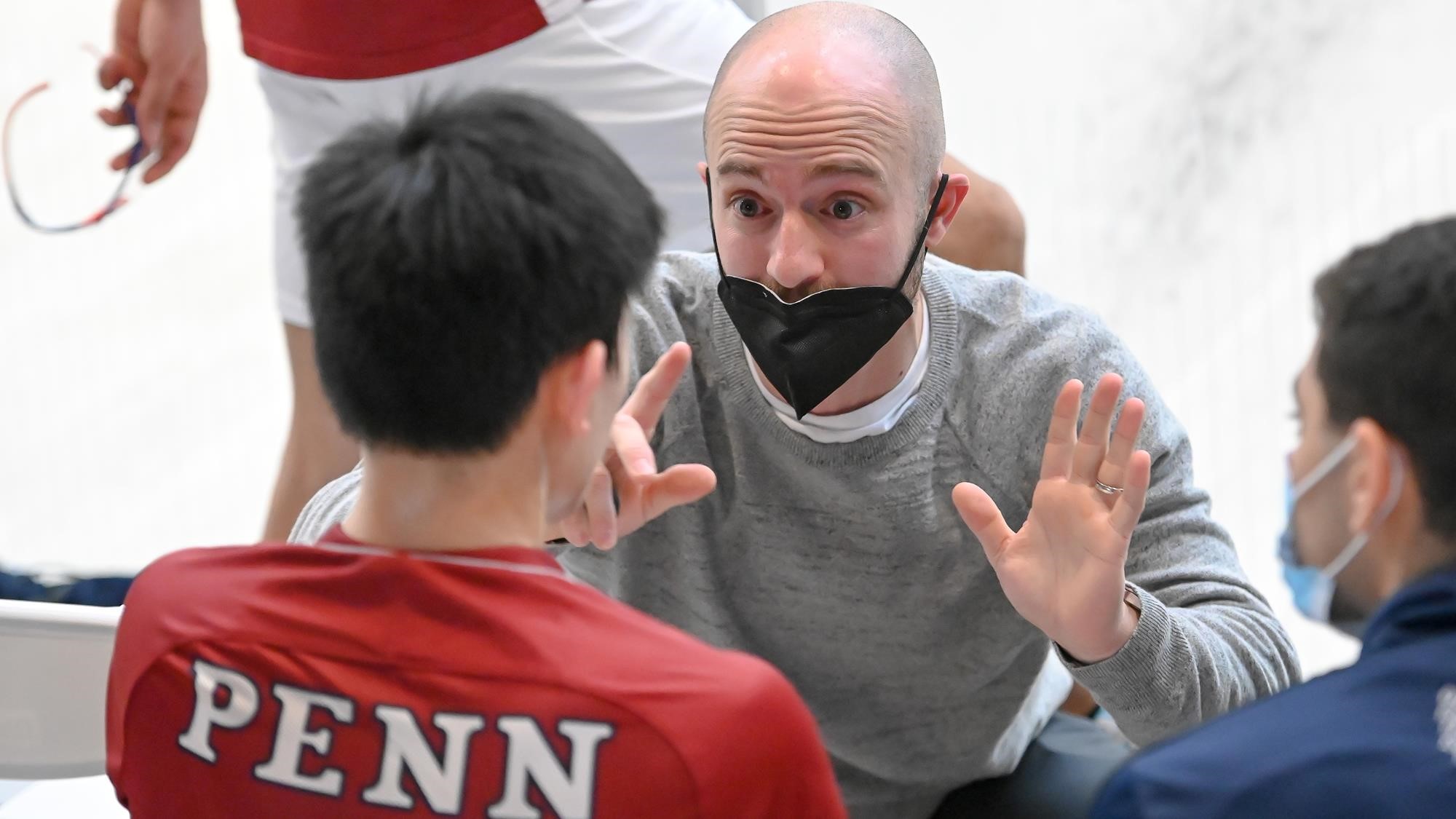 Gilly Lane, wearing a mask, kneels down ans speaks to two players.