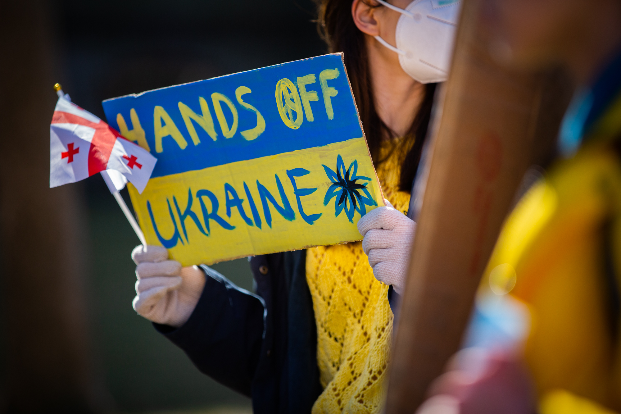Hands holding a sign that reads HANDS OFF UKRAINE.