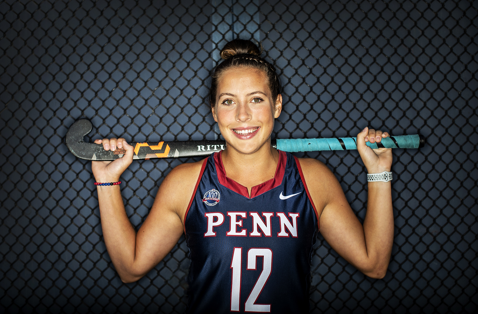 Banks holds her field hockey stick across her shoulders behind her neck.