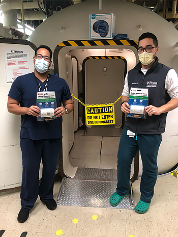Michael Tom, (left) outside of the hyperbaric chamber with Jonathan Romero, holding the carbon monoxide detectors they’ll be distributing.