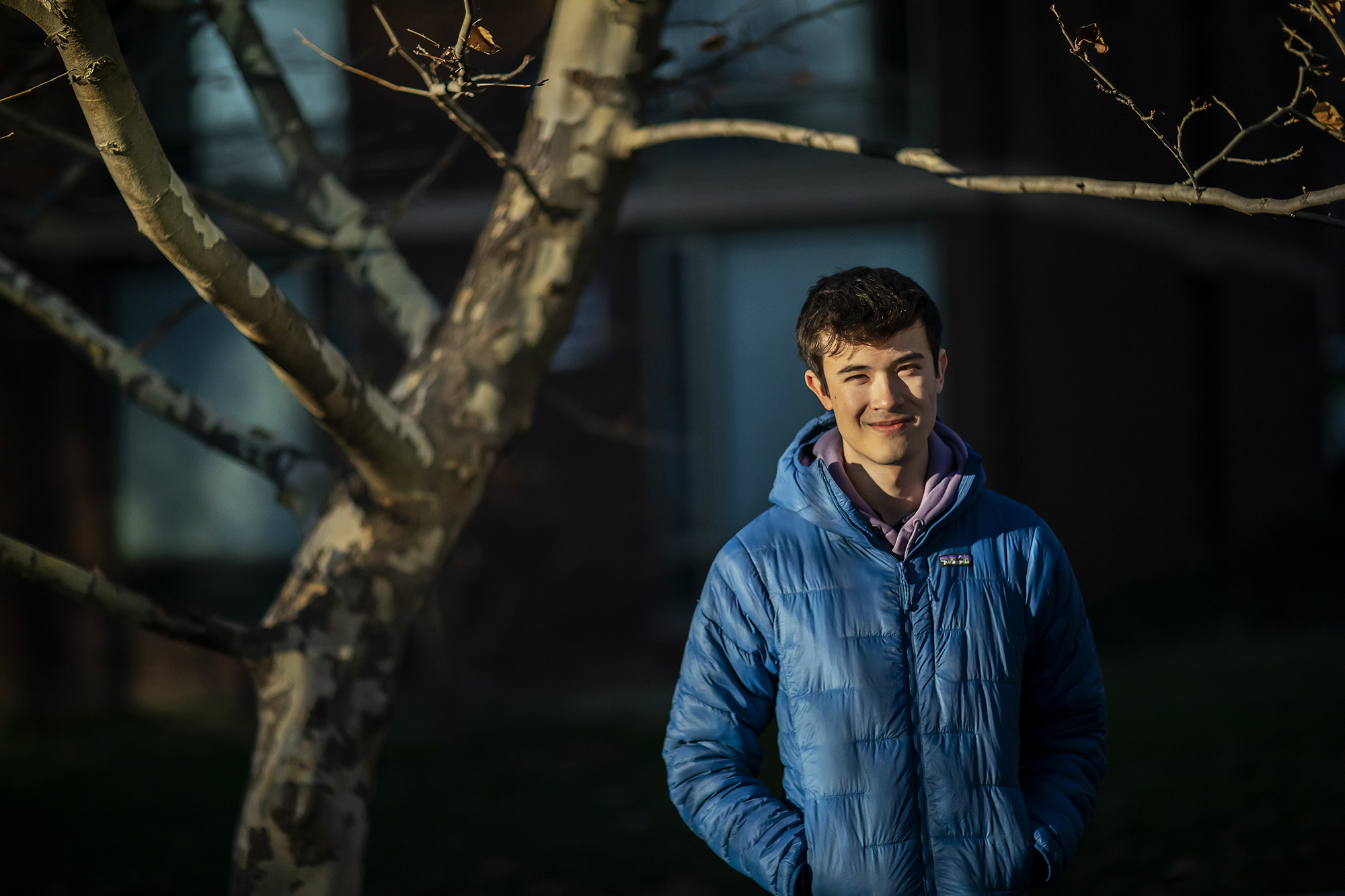 Man in blue jacket smiles next to bare tree
