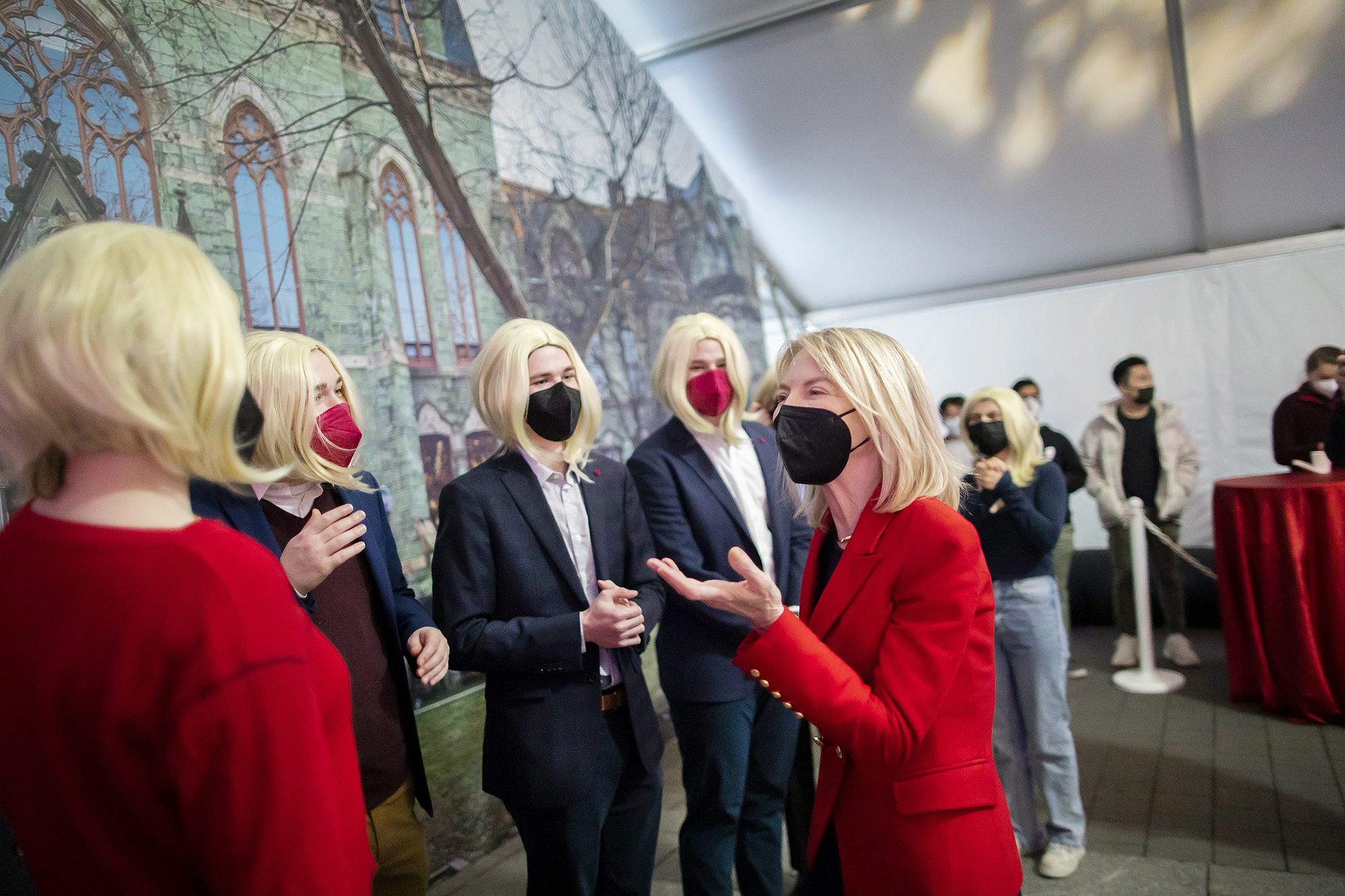 Penn President Amy Gutmann at a party talking with students wearing blonde wigs.