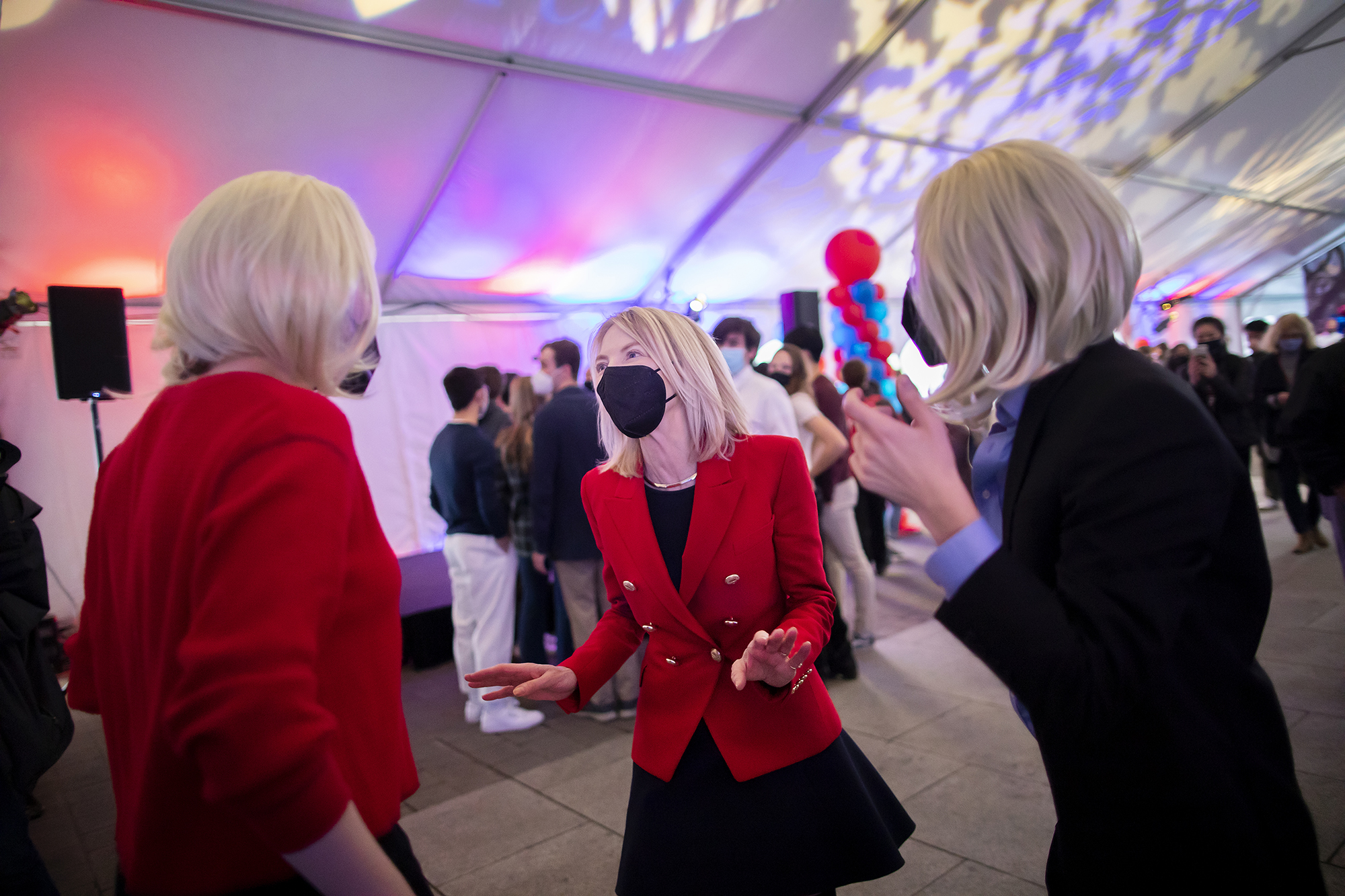 Penn President Amy Gutmann at a party talking with two students wearing blonde wigs.