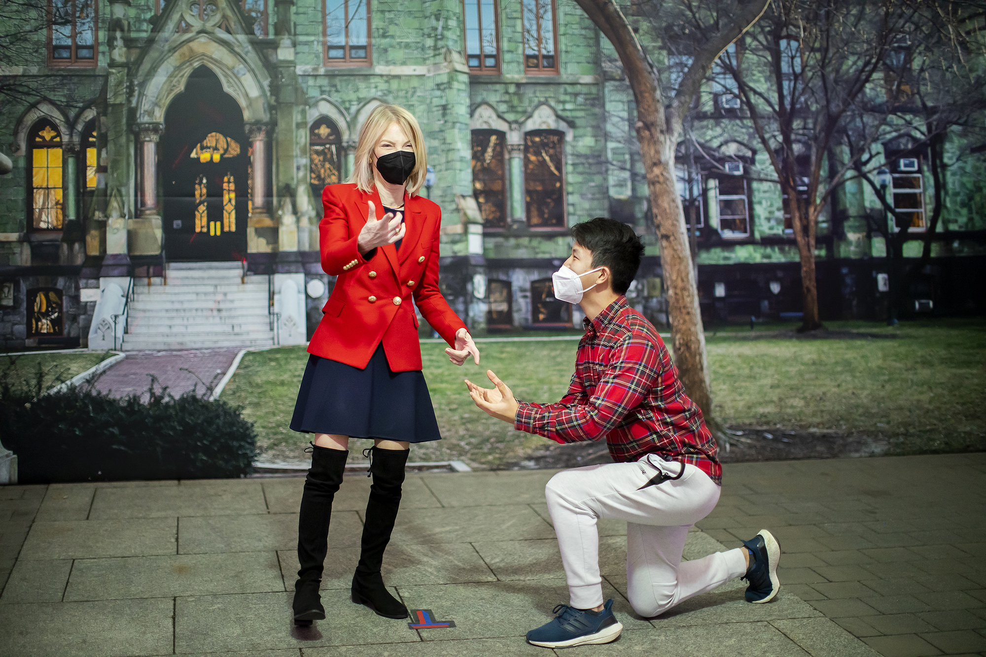 Penn President Amy Gutmann and a student on one knee next to her.