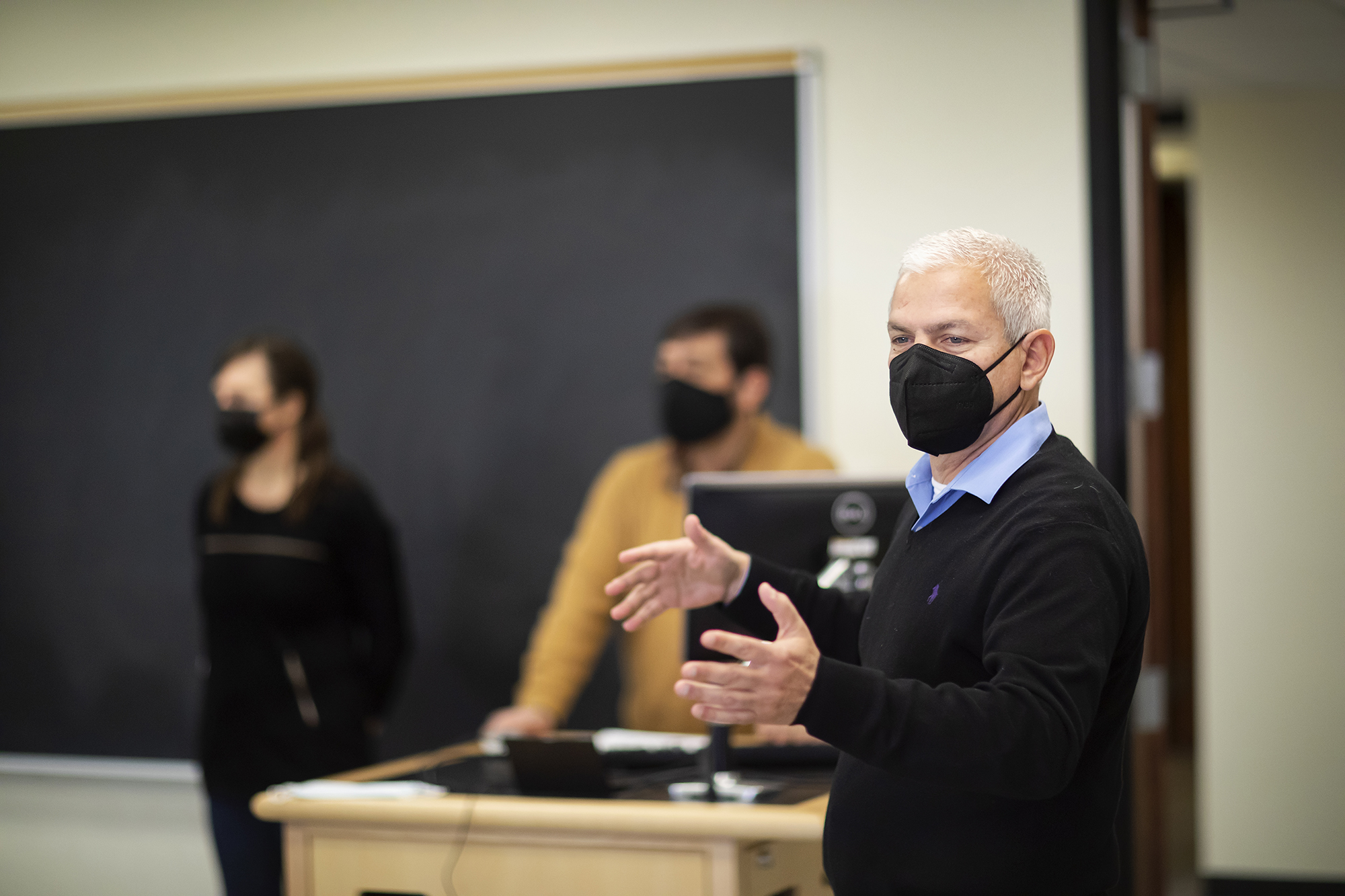 Emilio Parrado in a classroom gesturing as he speaks to the class. Two people are blurred behind in the background.