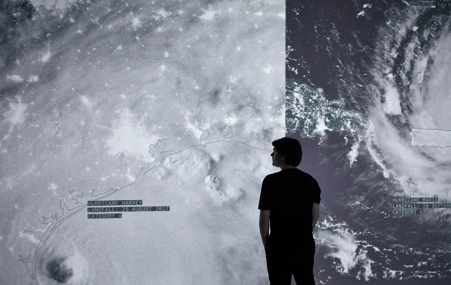 Person standing in front of two giant panels of film projected on the wall of NASA footage of a storm on planet Earth. 