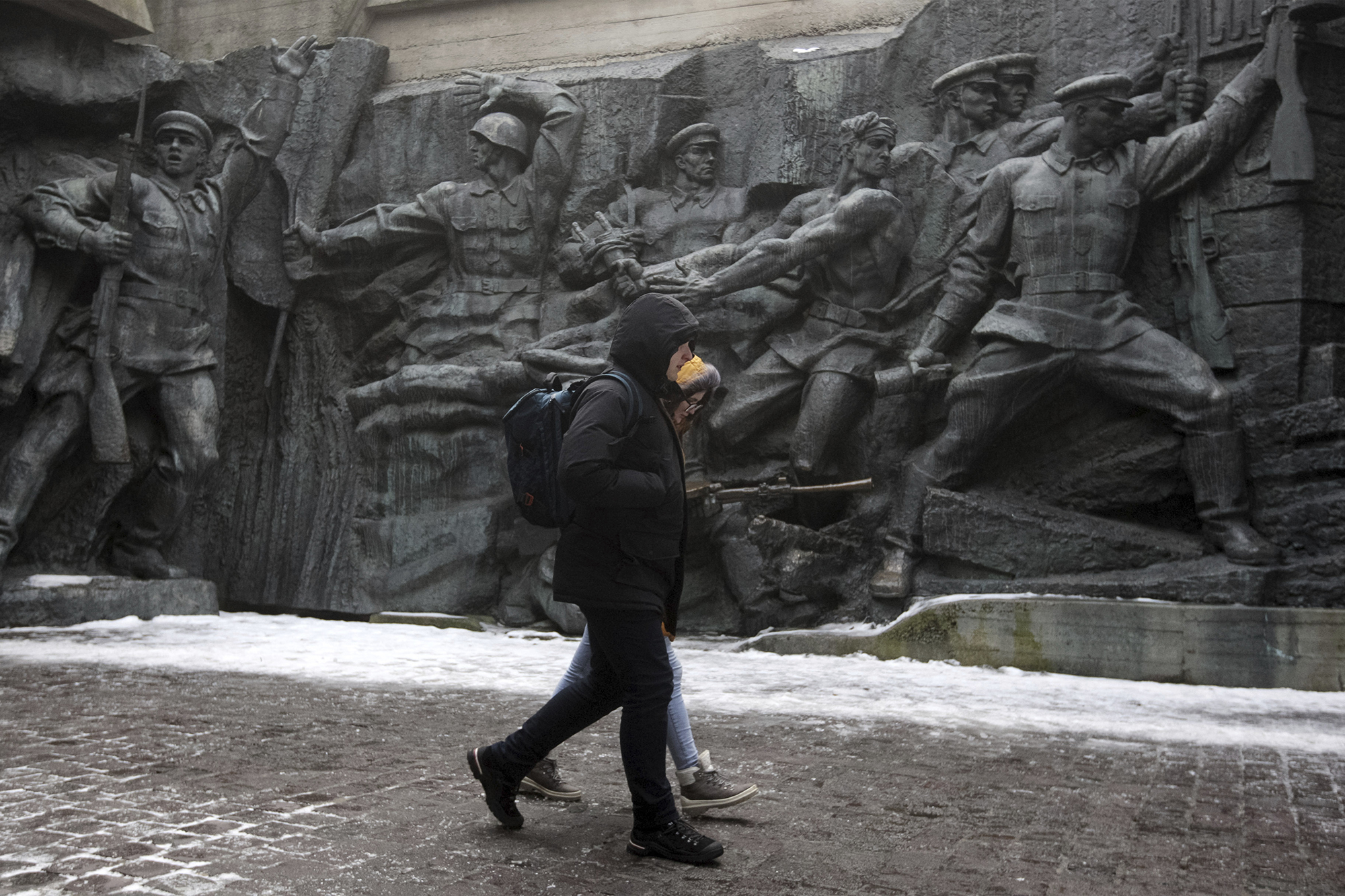 Two people walk in front of a wall engraved with scenes of WWII soldiers in Kyiv, Ukraine