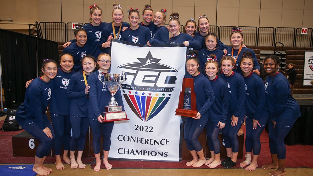 Members of the gymnastics team pose with the GEC Championship banner and trophies.