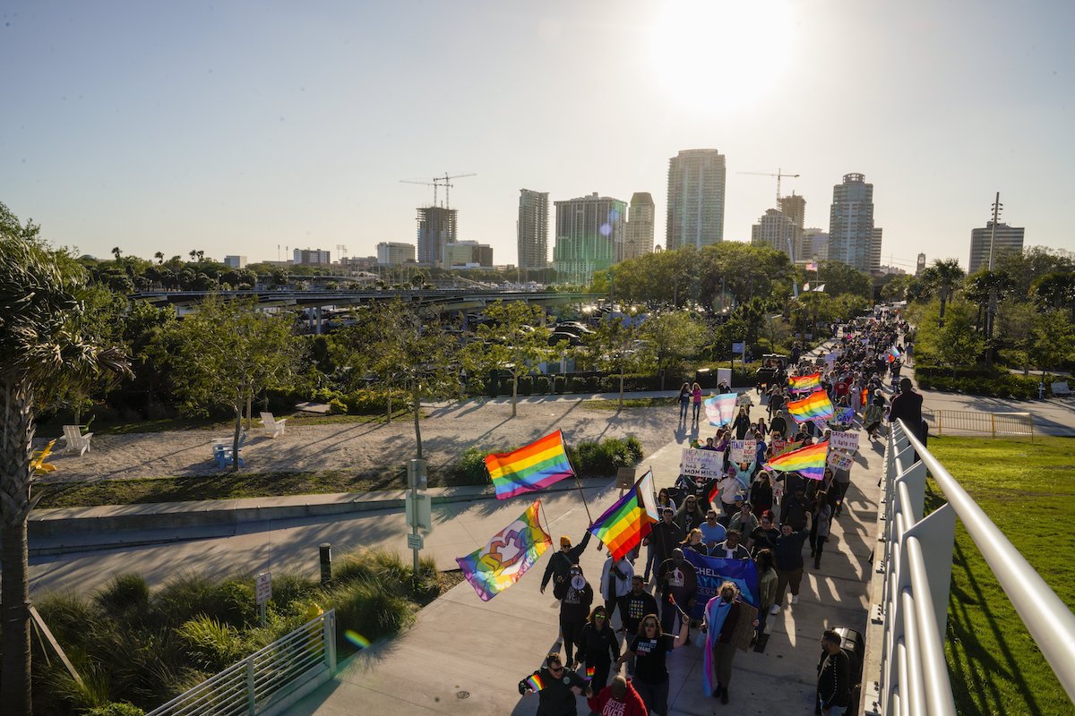 Marchers waving gay pride flags make their way long a boardwalk with the skyline of St. Petersburg, Florida, in the background