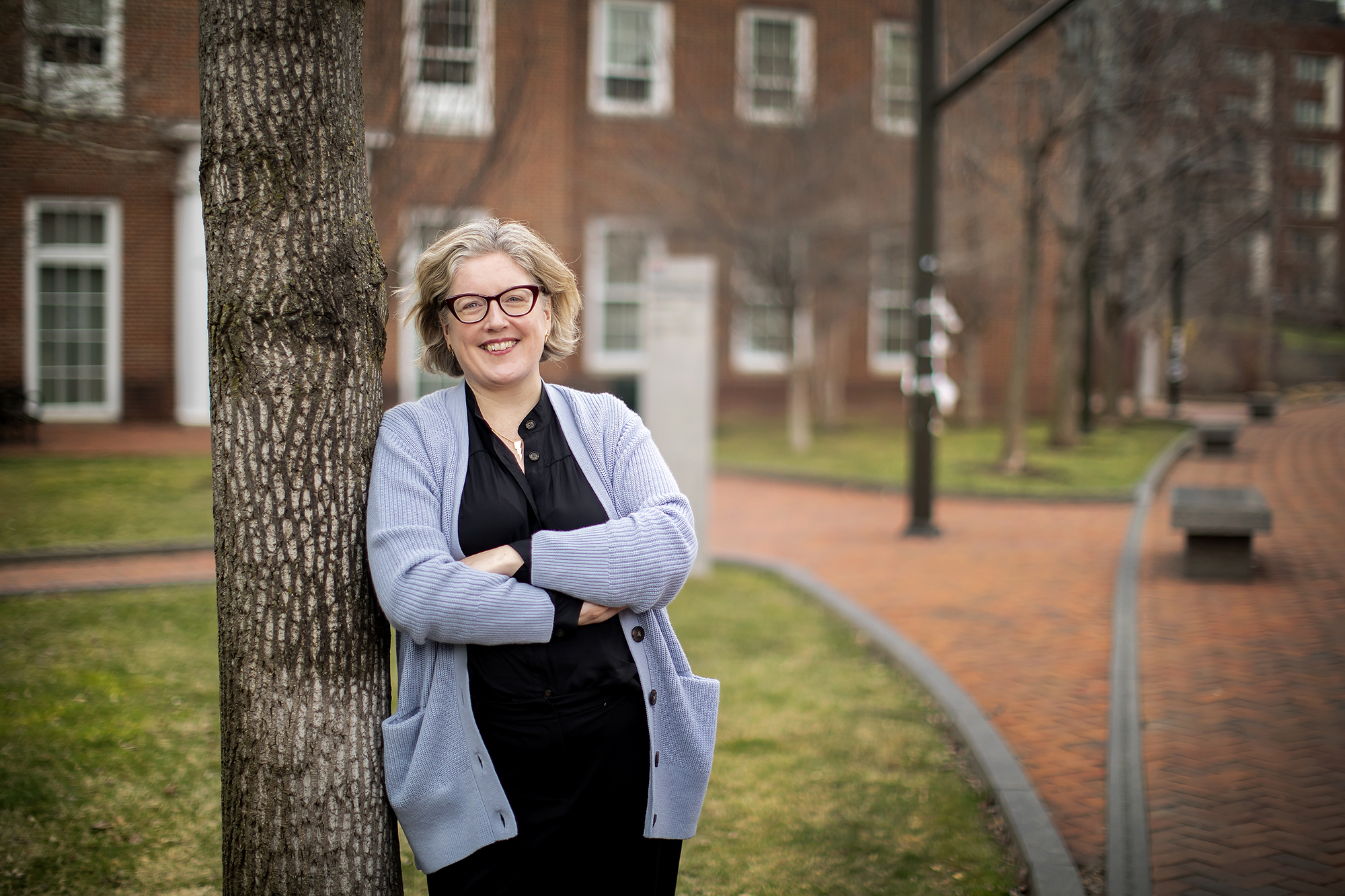 Emma Hart leans against a tree in front of the McNeil Center on Penn campus with her arms crossed, smiling at the camera