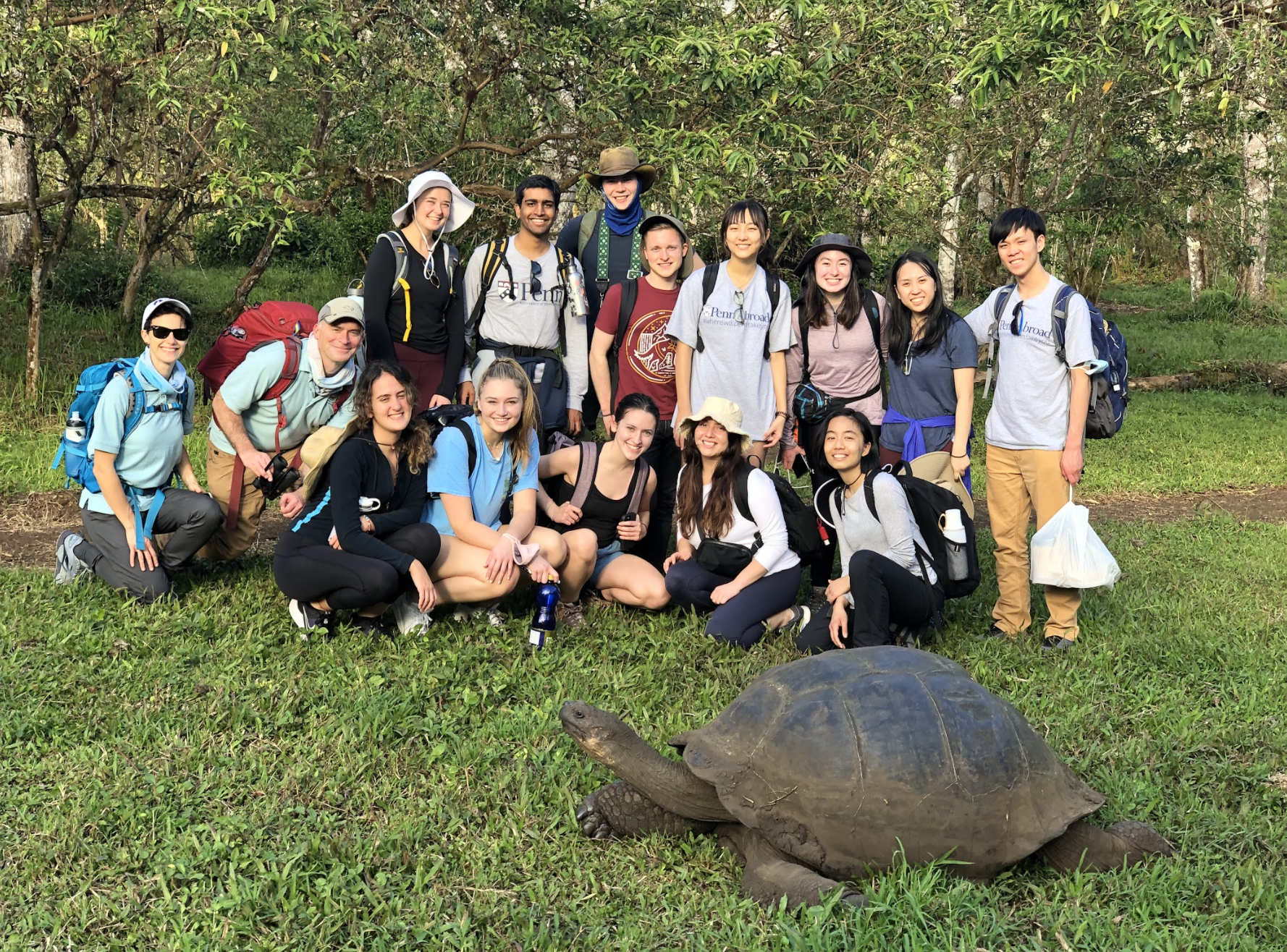 A group of Penn Abroad students in Galapagos smile for the camera as a turtle walks past them on the grass.