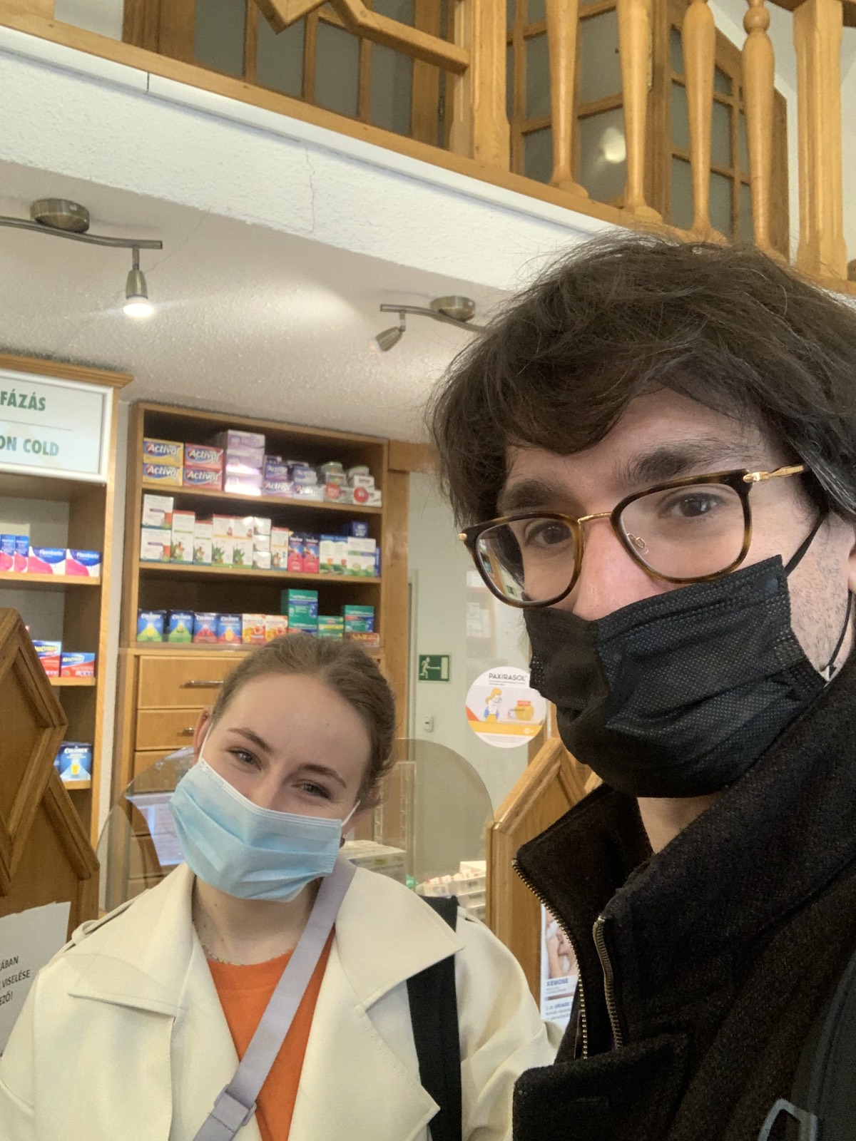 Two people wearing masks look at the camera inside a Budapest pharmacy