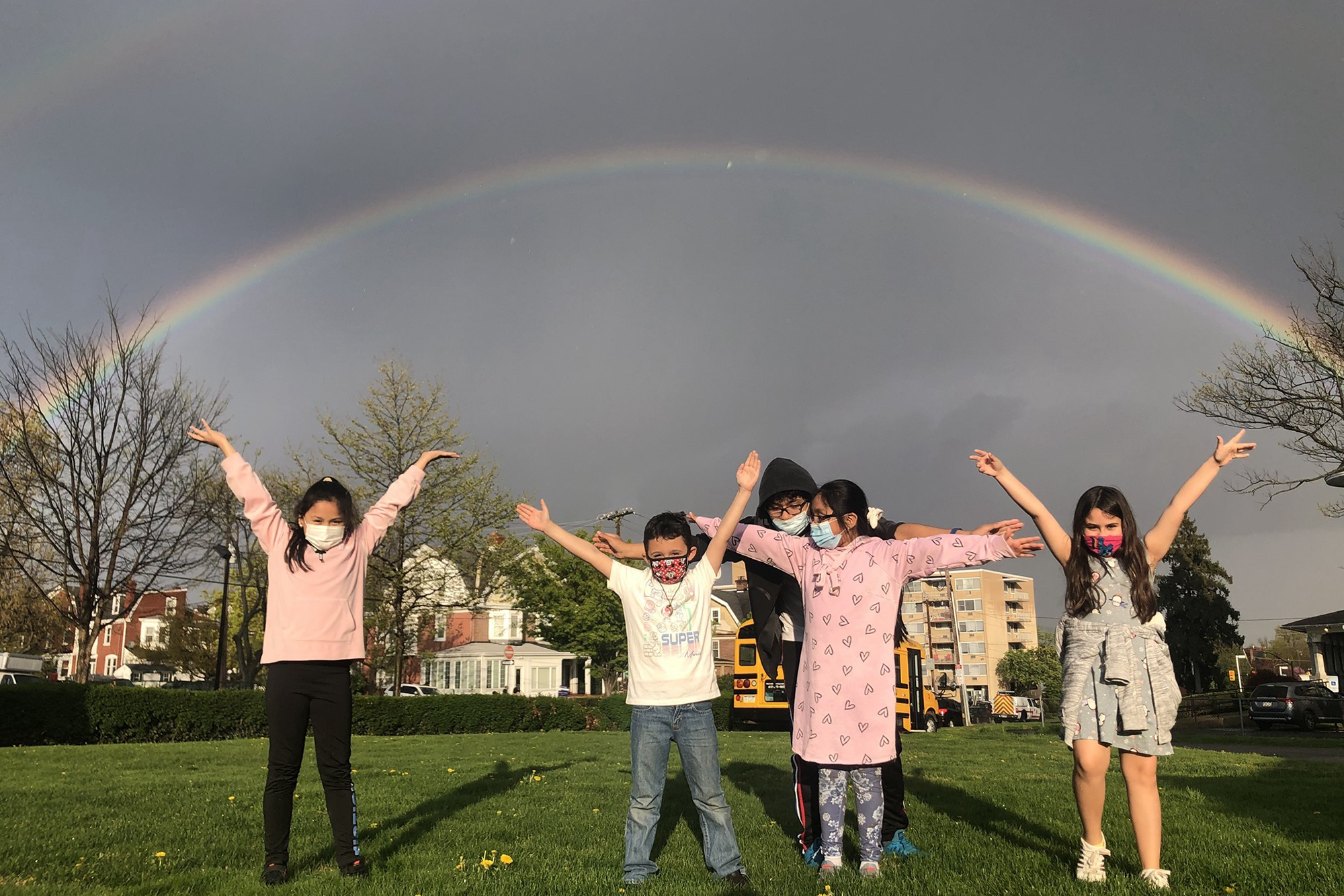 Children raising their hands with a rainbow in the background