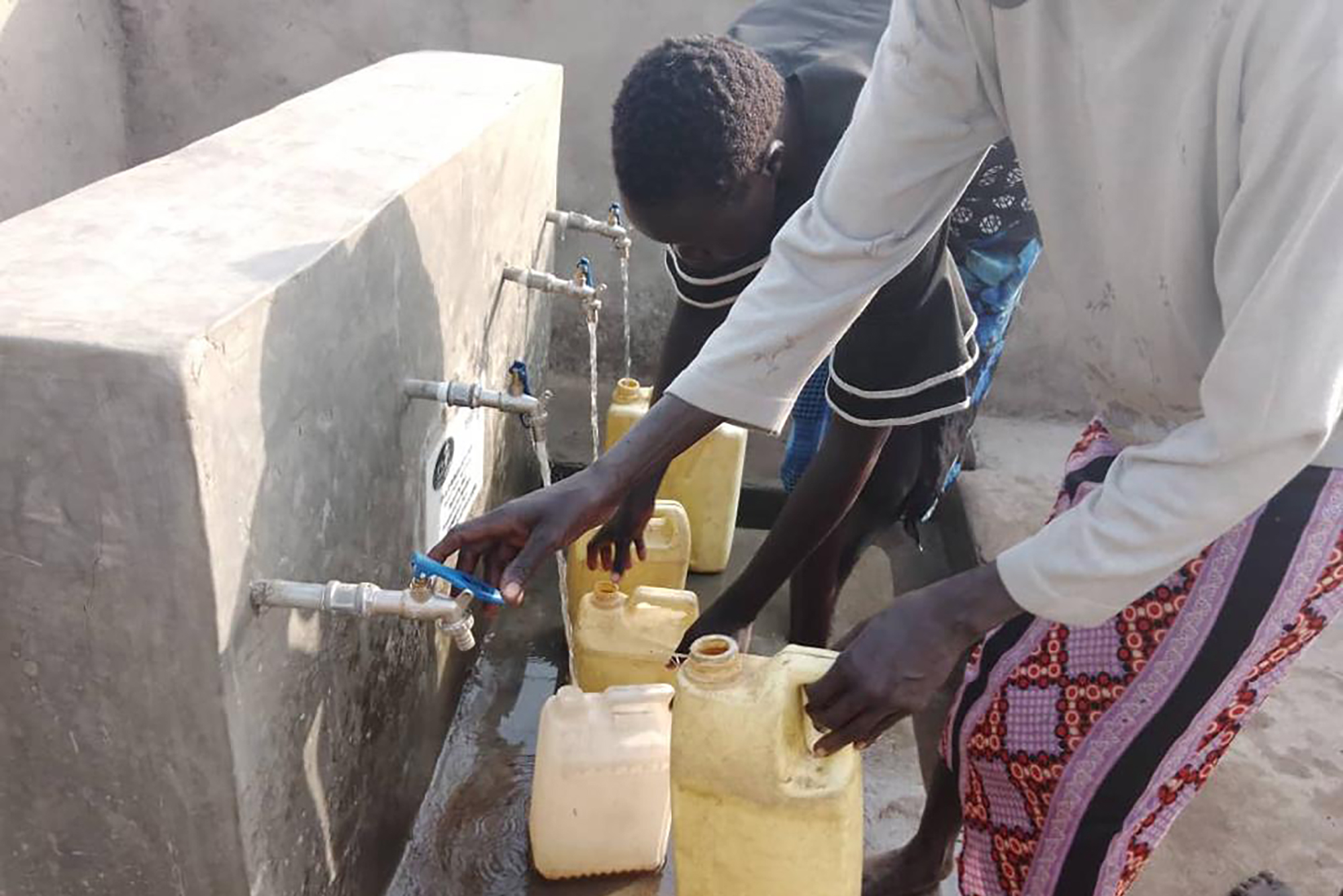 Two people in Uganda fill jugs from water taps.