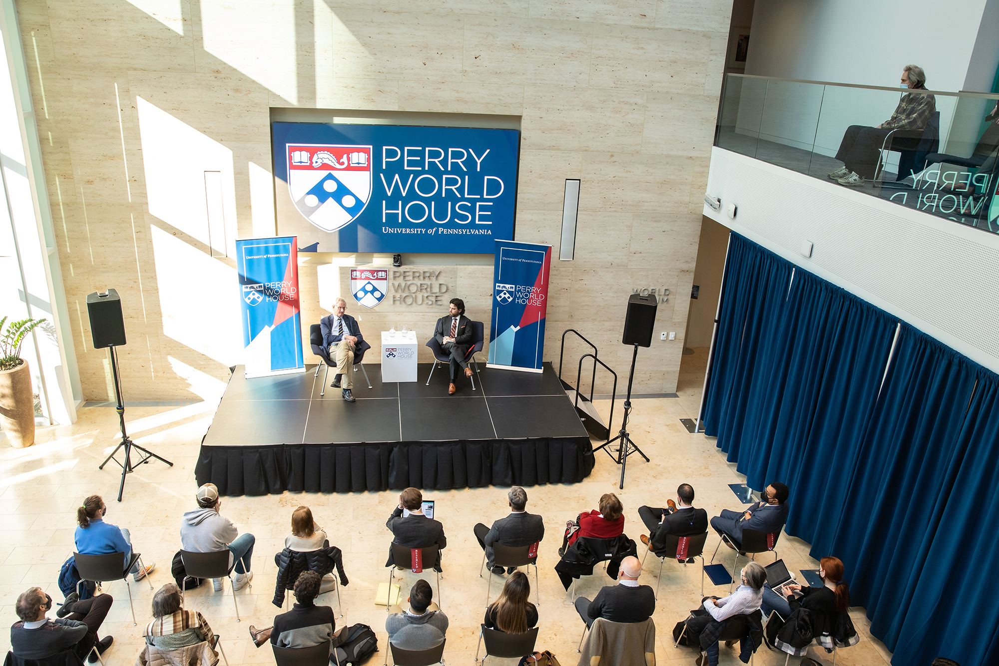 Carl Bildt and Clay Risen are seen on a stage speaking in front of a group of seated people at Perry World House