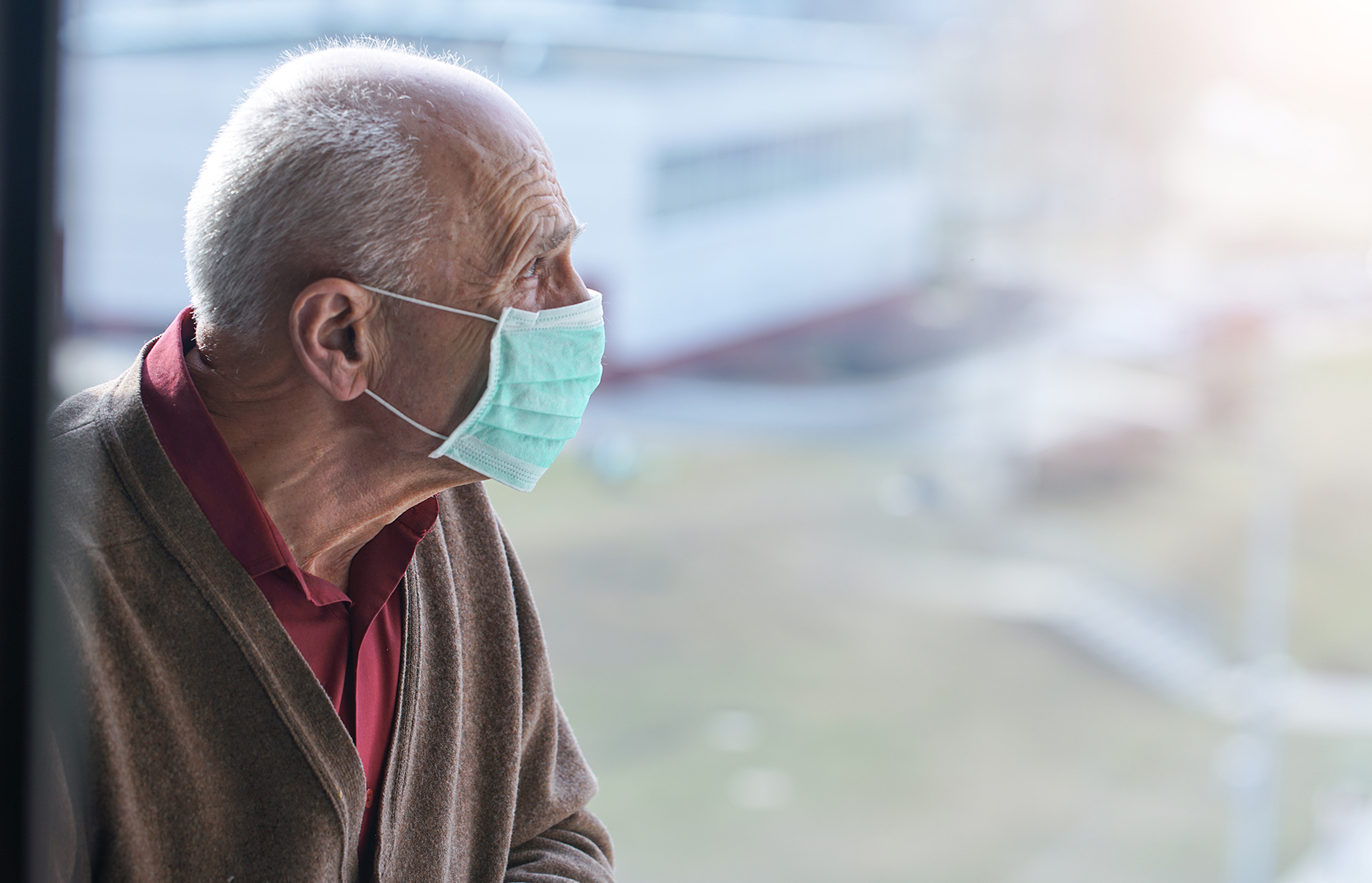 Elderly person sitting alone wearing a face mask.