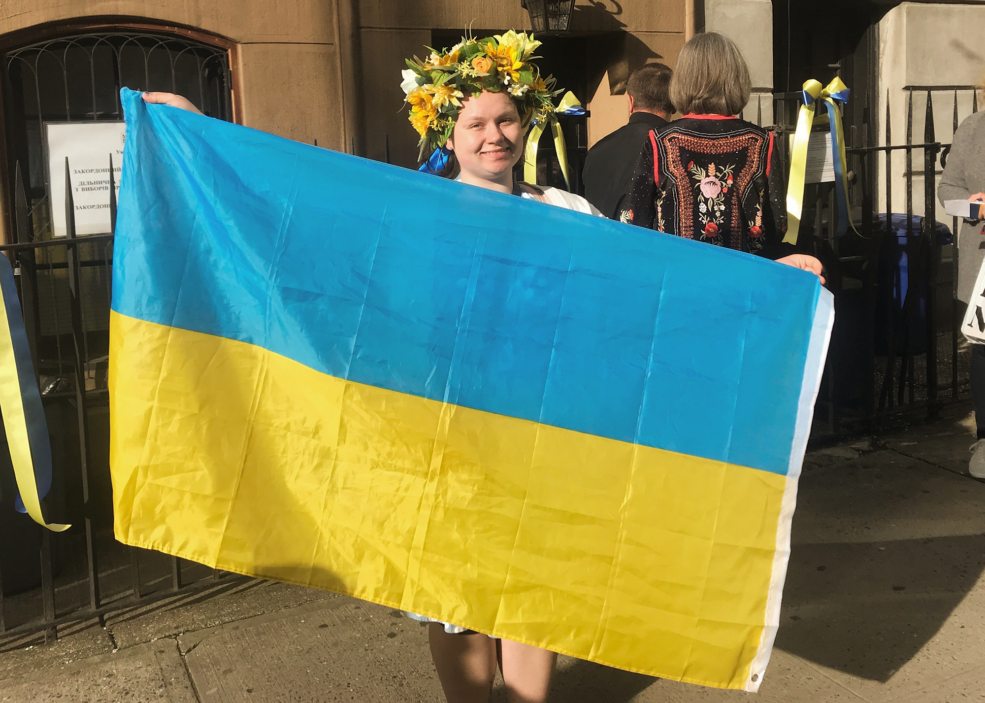 Alice Sukhina in Ukraine holding a large Ukrainian flag wearing a flower crown.