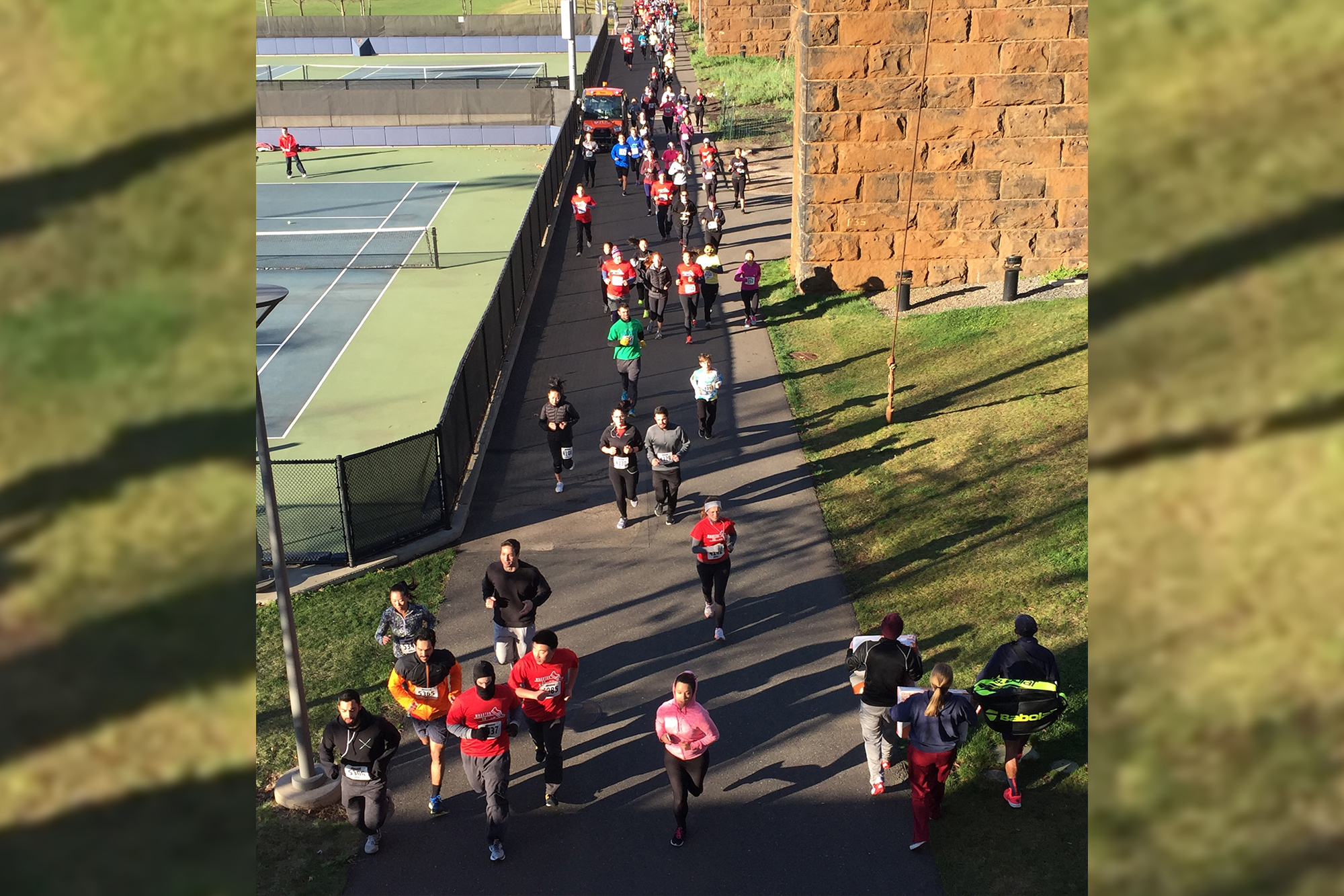 Aerial view of runners along a street with tennis courts on one side.