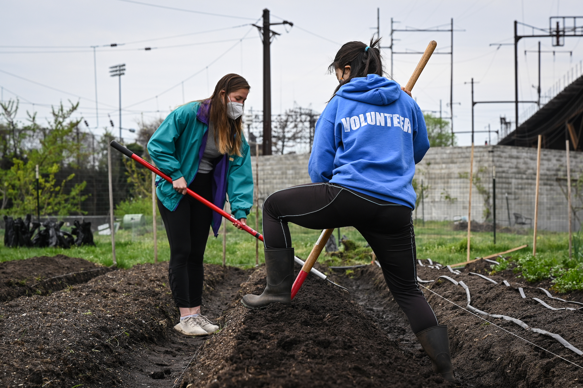 Two people with farming tools work in a field in an urban environment