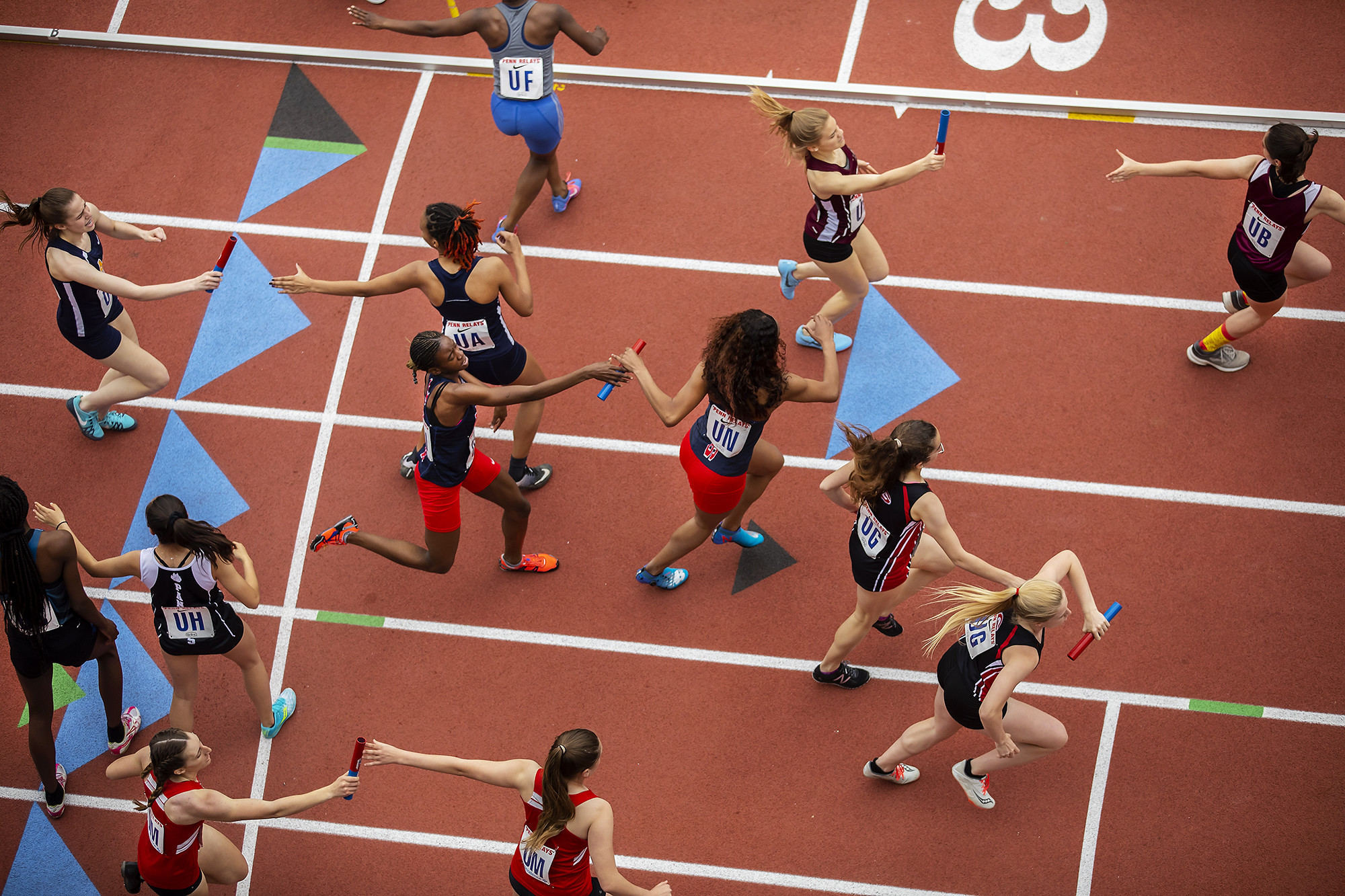 Relay runners pass batons during the Penn Relays at Franklin Field.