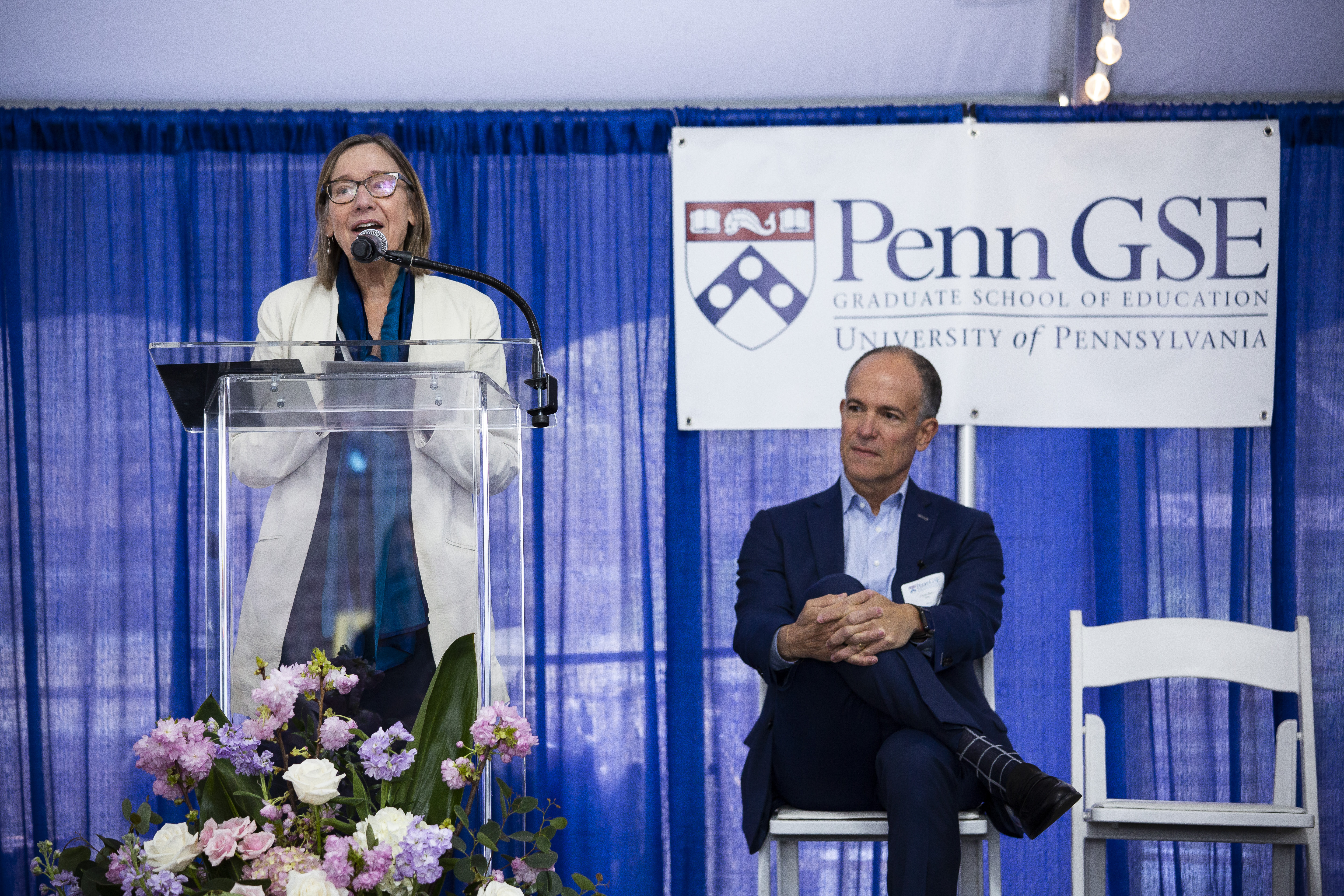 Dean Grossman speaking at podium with Doug Korn sitting to her right