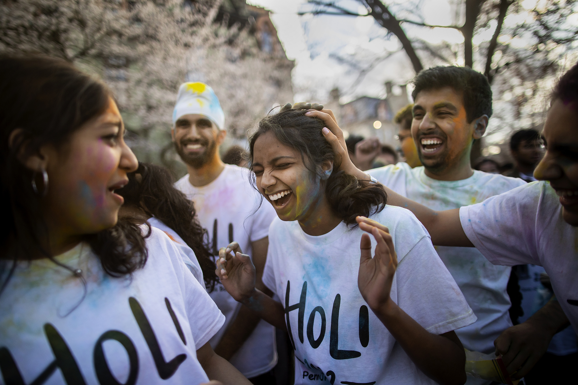 A crowd of people on College Green celebrating Holi with colorful powders.