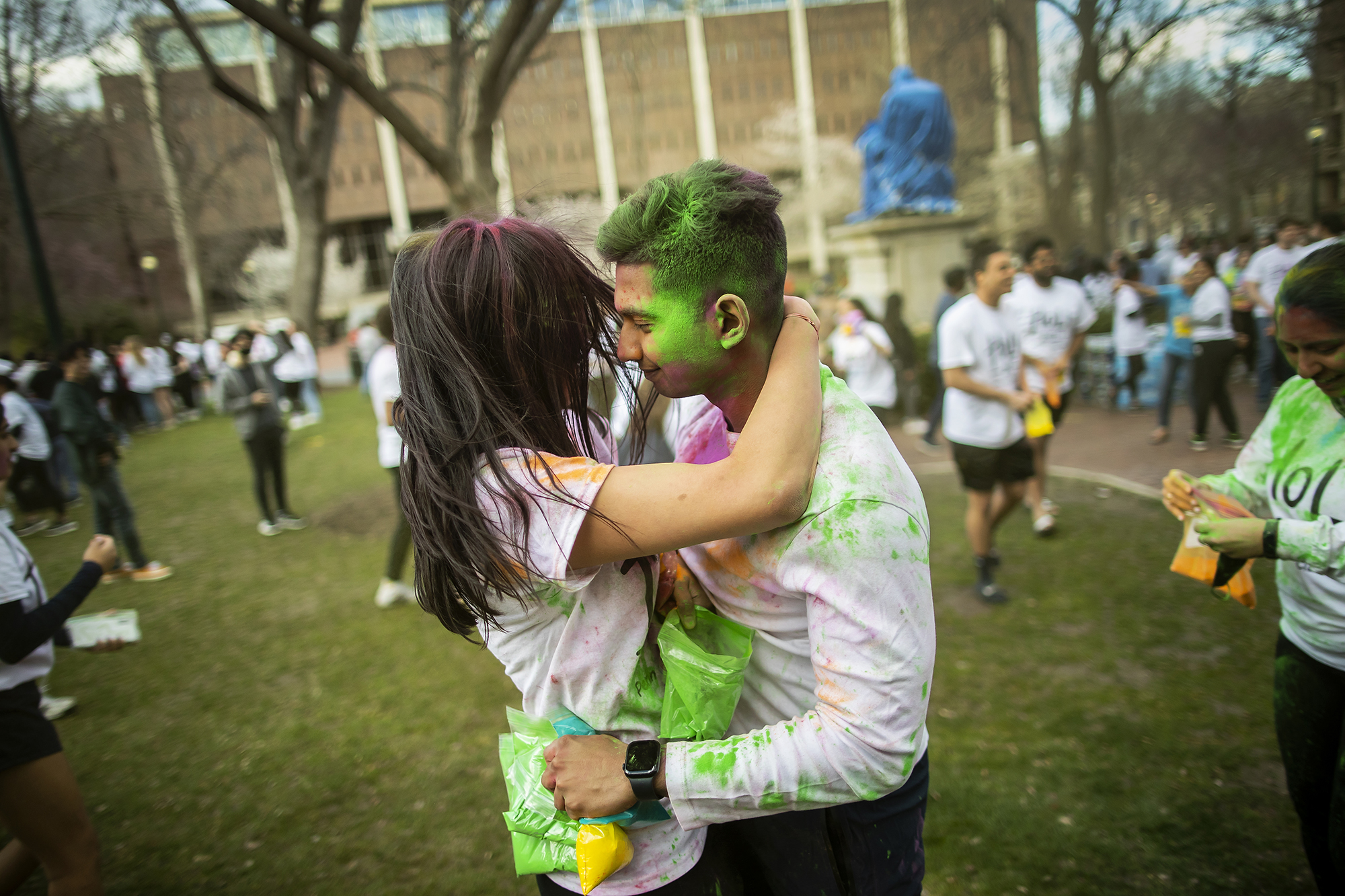 A couple embracing on College Green while celebrating Holi covered in colorful powder.