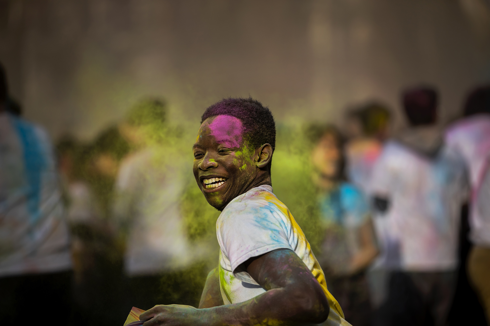 A person covered in colorful powder smiles.