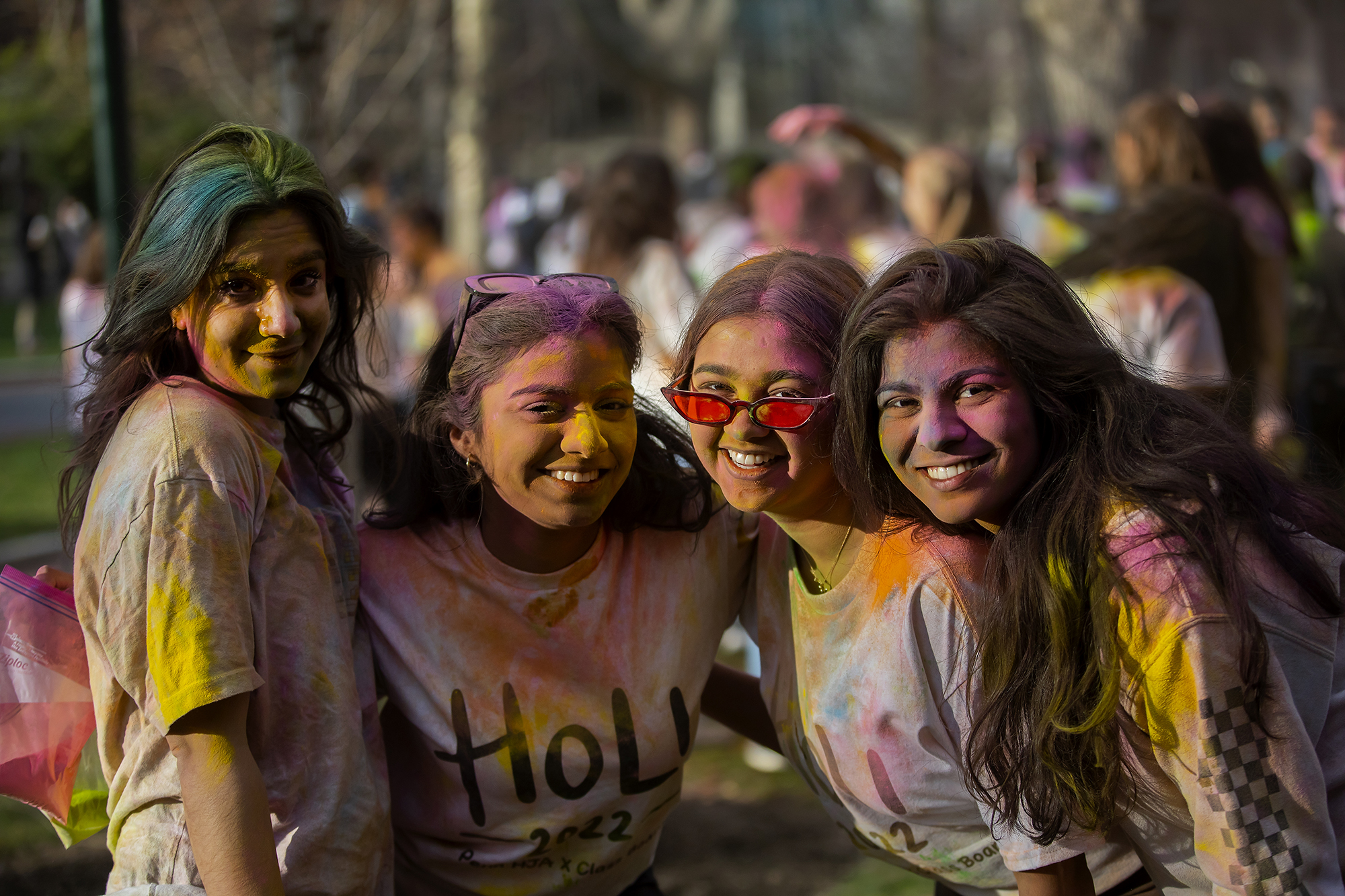 Four people on College Green covered in colorful powder celebrating Holi.