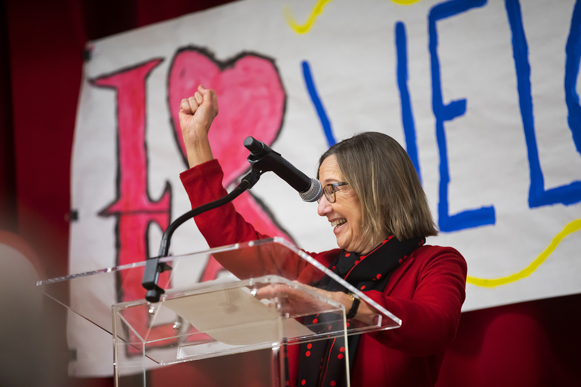 Dean Pam Grossman smiles and holds one arm up at podium